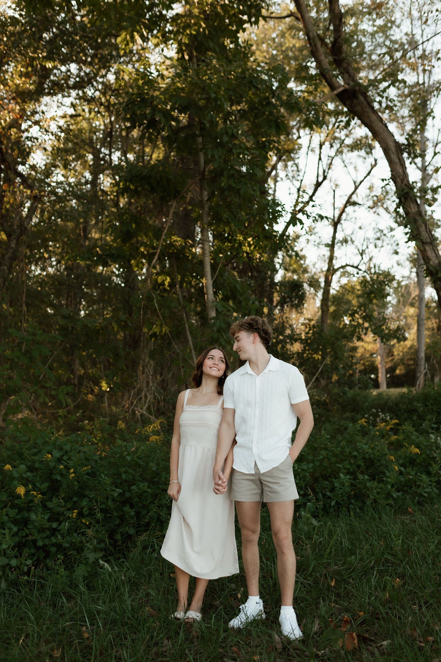Young couple holding hands and exchanging glances in a sunlit forest clearing at golden hour.