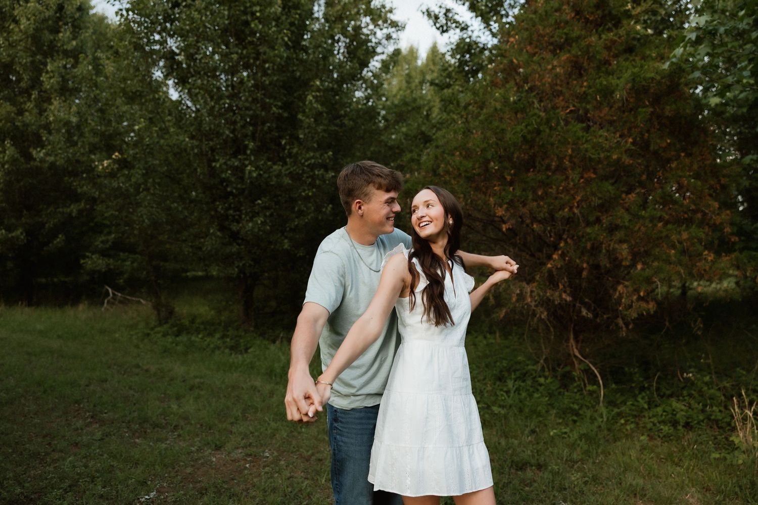 A couple holds hands and smiles at each other in a lush green park setting.