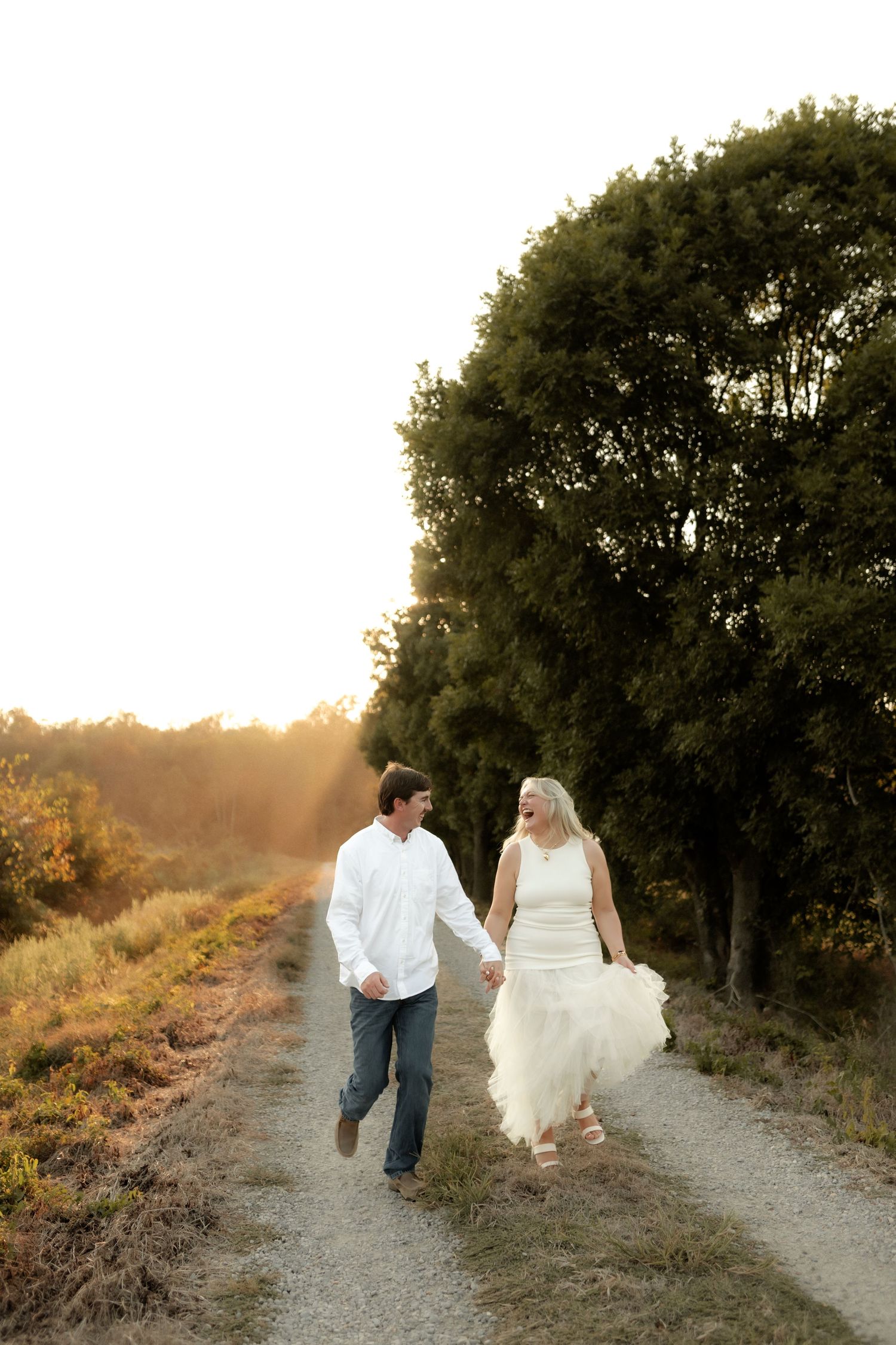Happy couple walking hand in hand down a sunlit gravel path surrounded by nature.