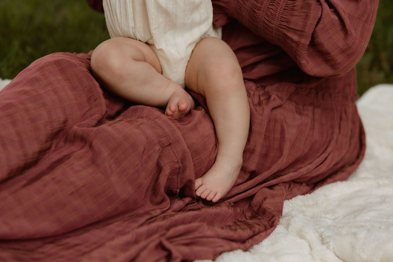 Close-up of baby feet resting on mother's rust-colored dress.