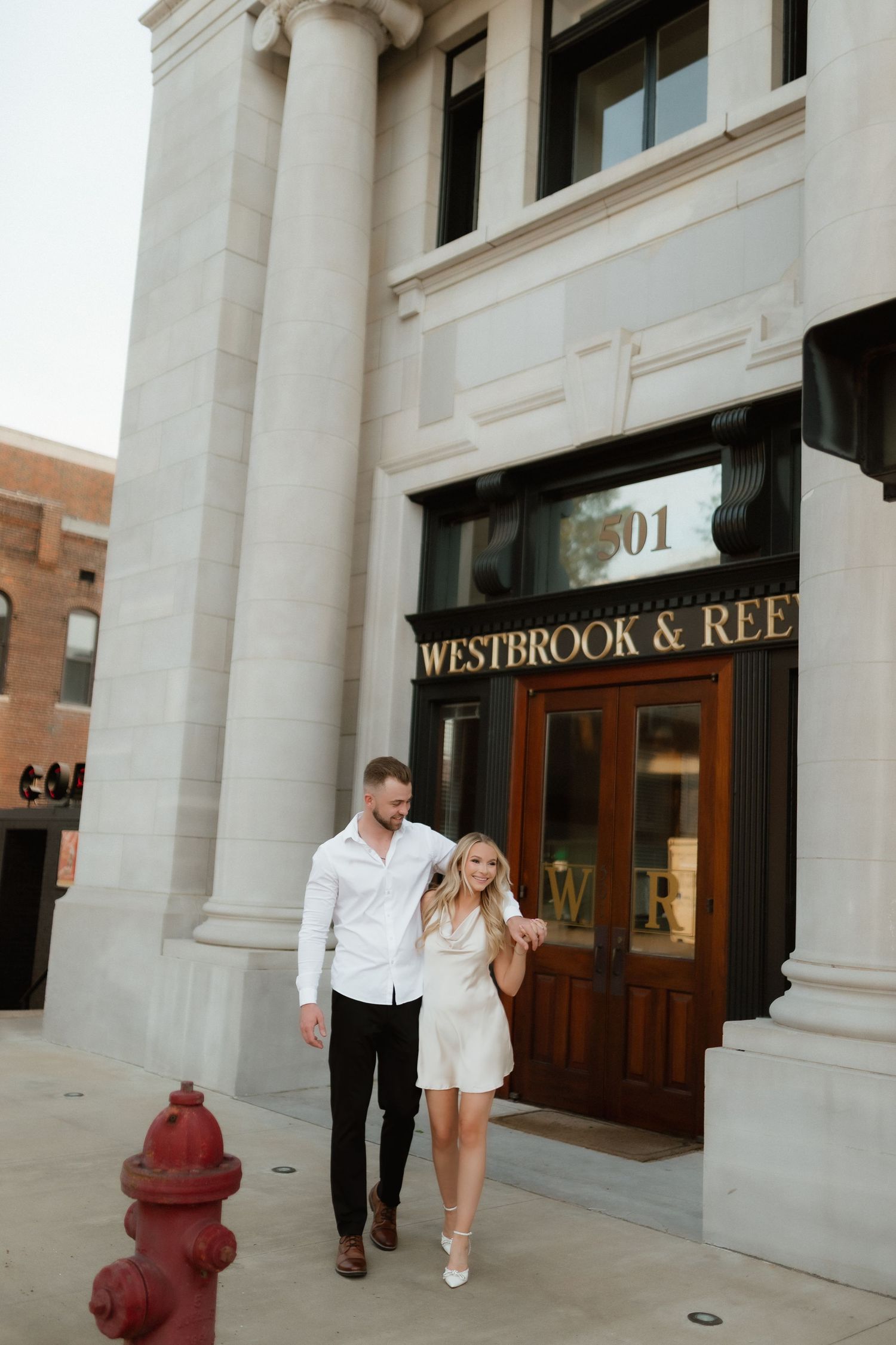 Stylish couple walking hand in hand outside Westbrook and Reed building entrance with white columns.