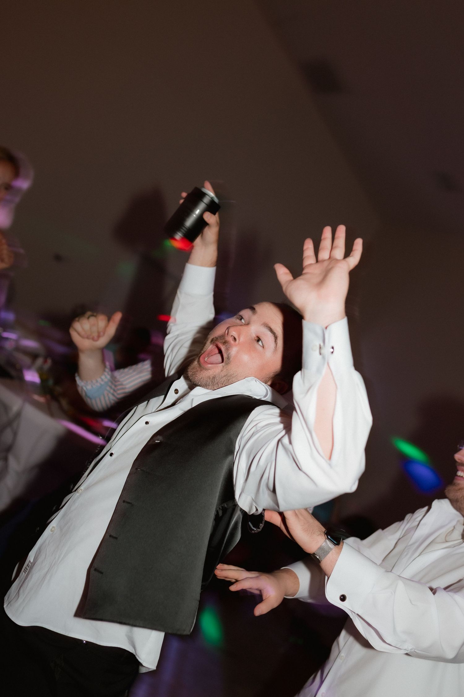 Groomsman dancing enthusiastically with arms raised at wedding reception celebration.