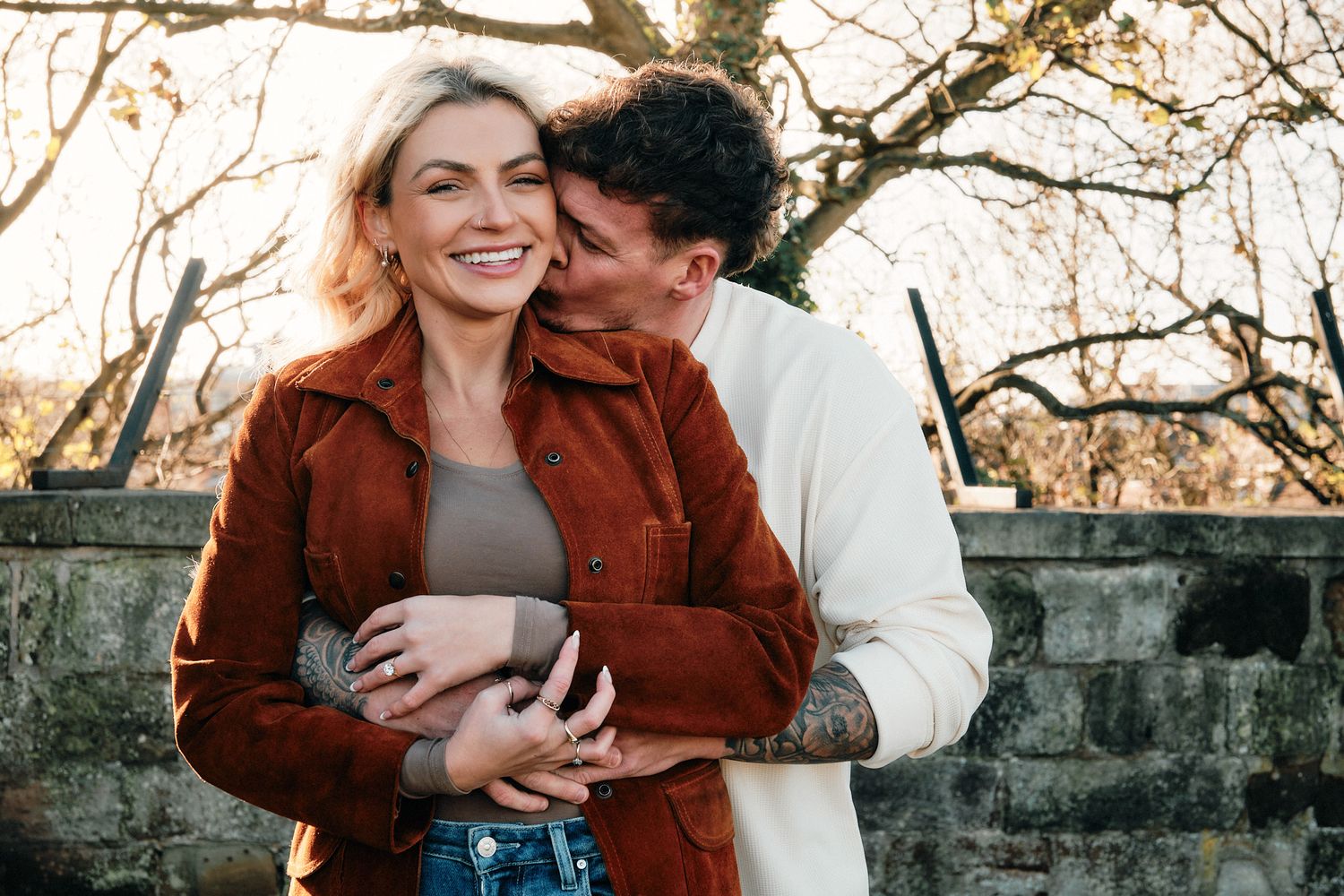 Couple embracing outdoors against stone architecture during golden hour.