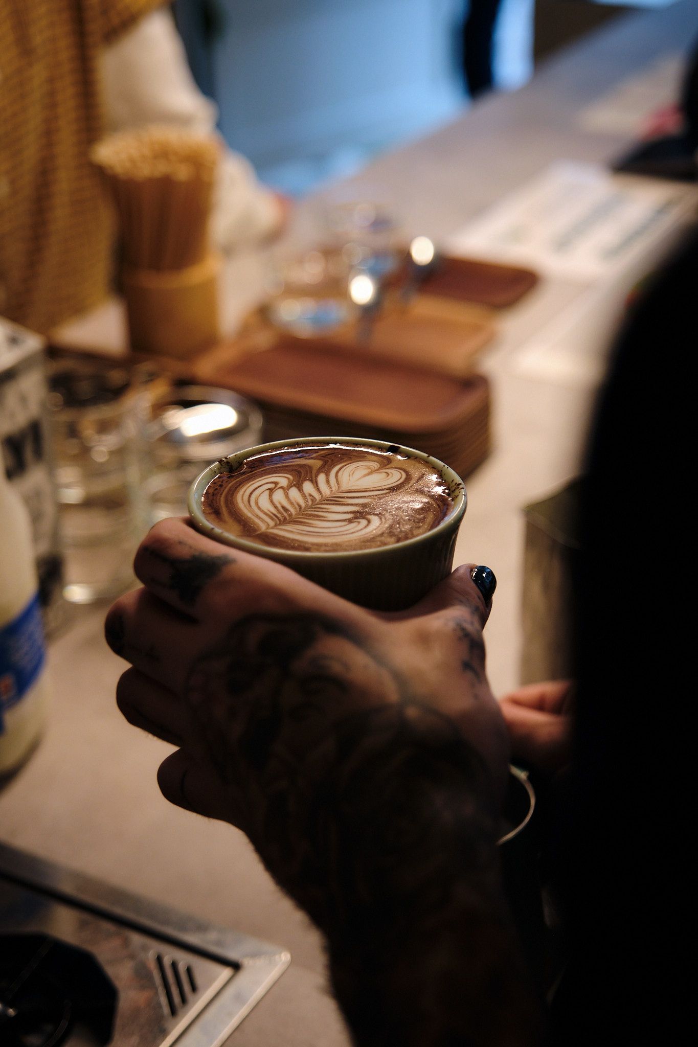 Hands holding a cup of coffee with detailed latte art pattern visible from above.
