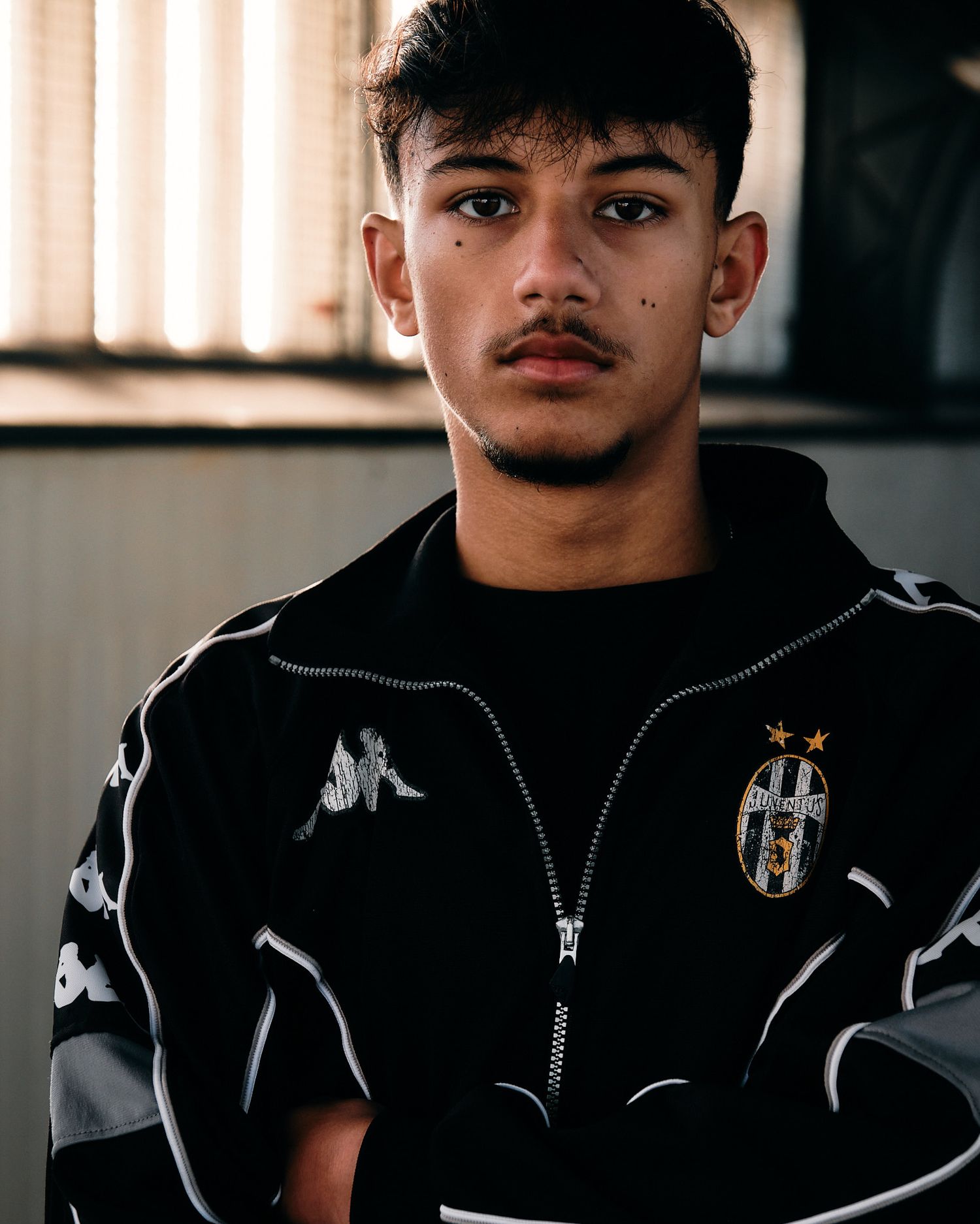 Person in black Juventus Kappa jacket posing against light background.