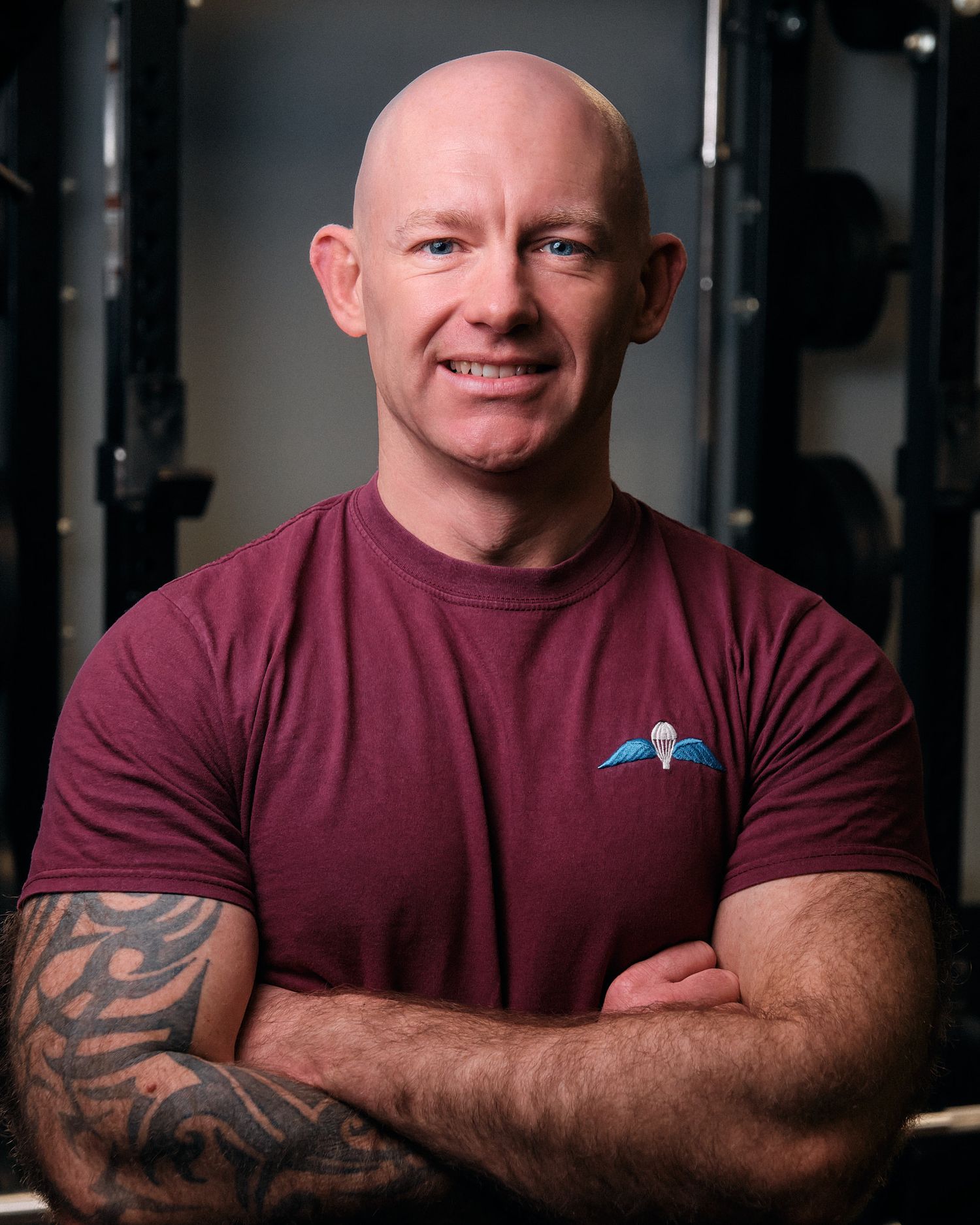 A muscular man in a burgundy t-shirt with tattoos poses in a gym setting across multiple similar photos.