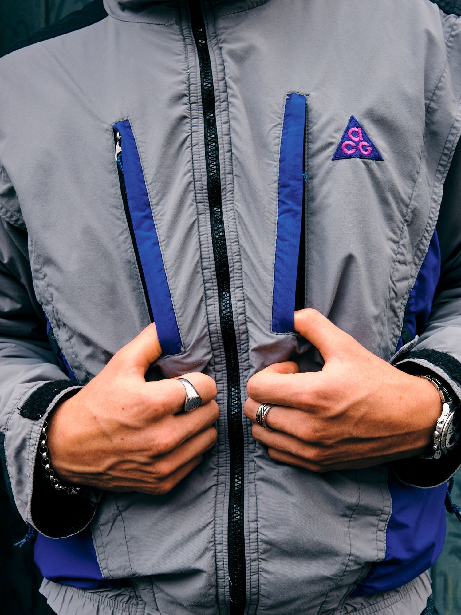 Hands showing details of a gray and blue athletic jacket with zipper closure.