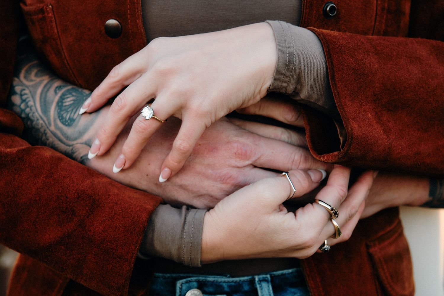 Close-up shots of hands with rings and tattoos against a burgundy background.