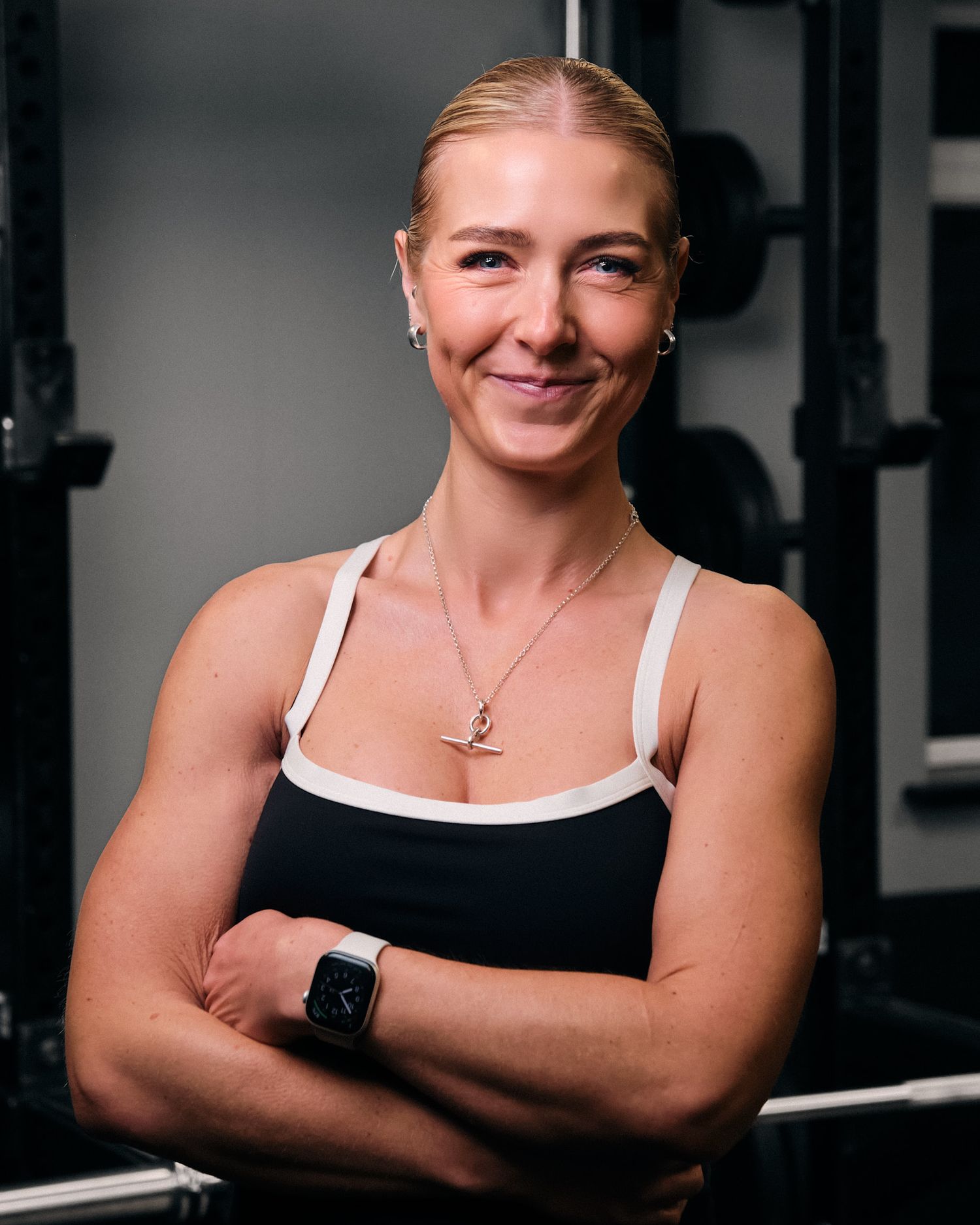 Athletic woman in black and white workout top smiles with crossed arms at fitness center.