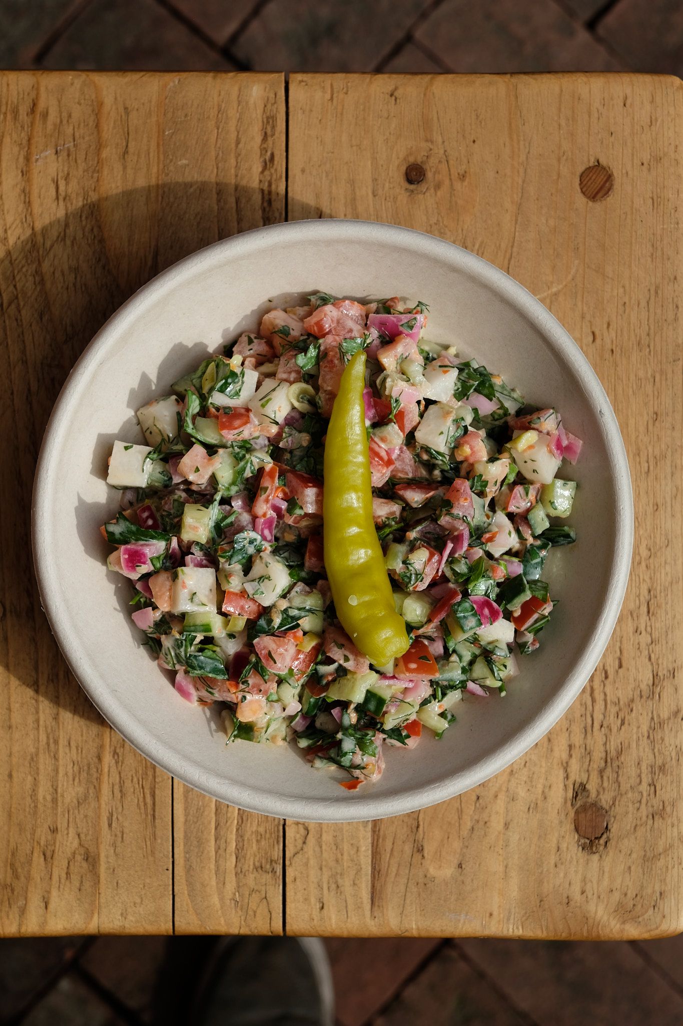 Colorful chopped Mediterranean salad with yellow pepperoncini on wooden surface.