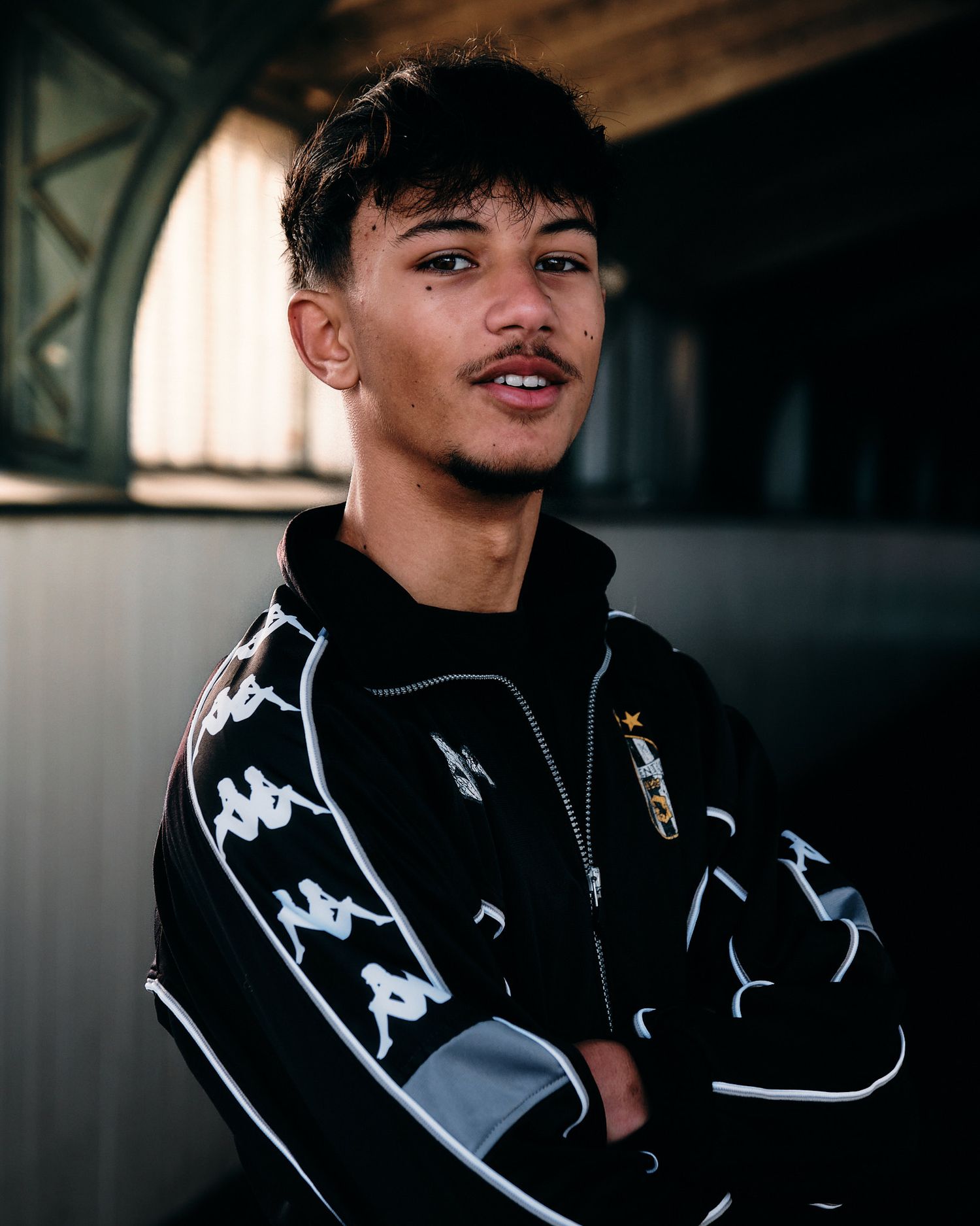 Athletic model wearing black Kappa tracksuit jacket with white trim in indoor setting.
