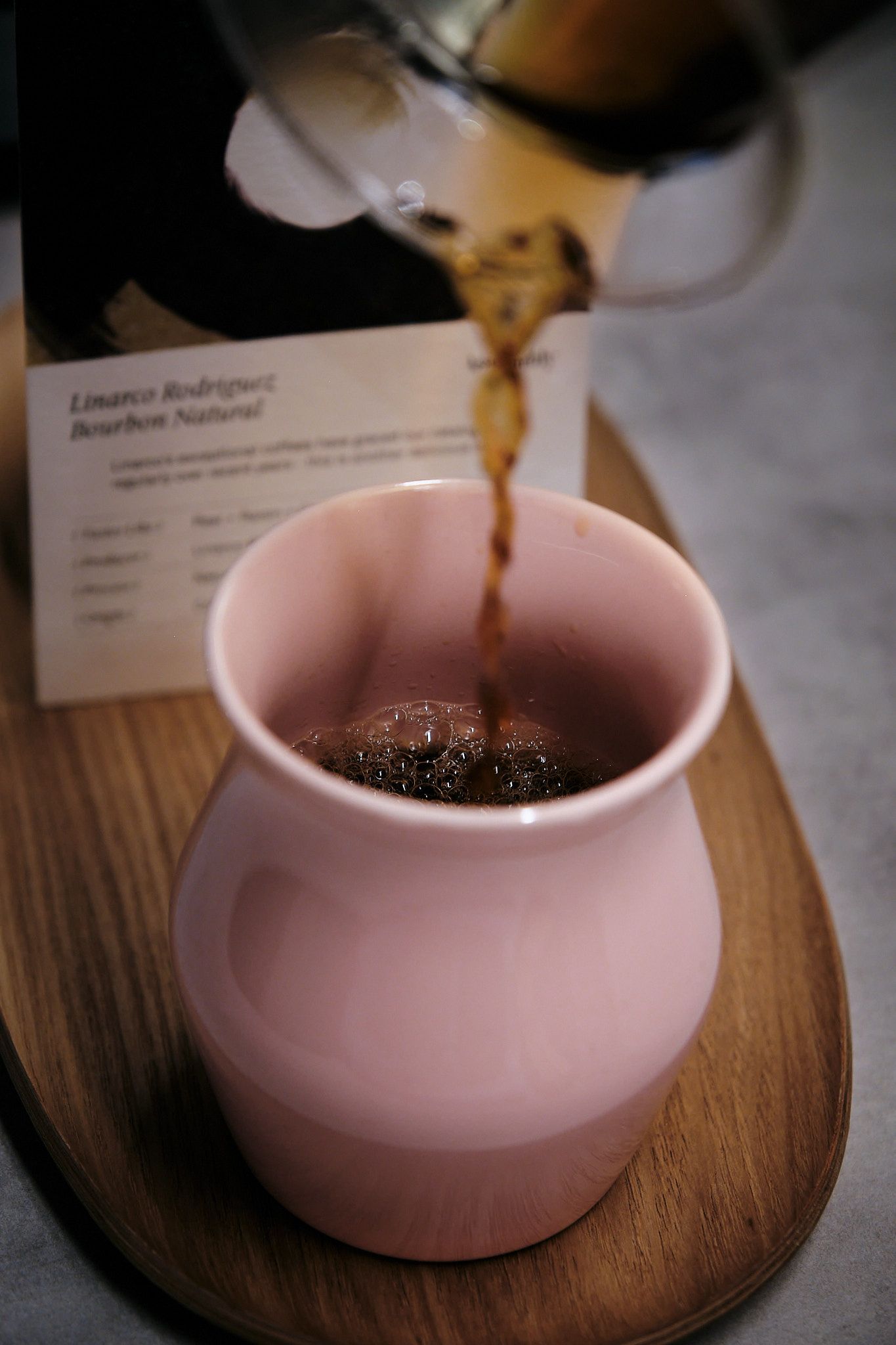 Fresh coffee streams into a pink ceramic cup on a wooden serving board.