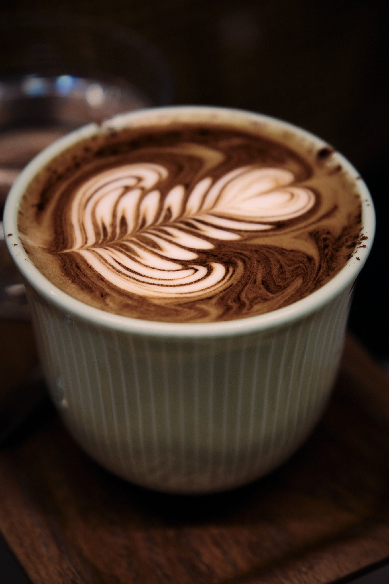 A white ceramic bowl containing latte art with intricate heart and leaf patterns in the foam.