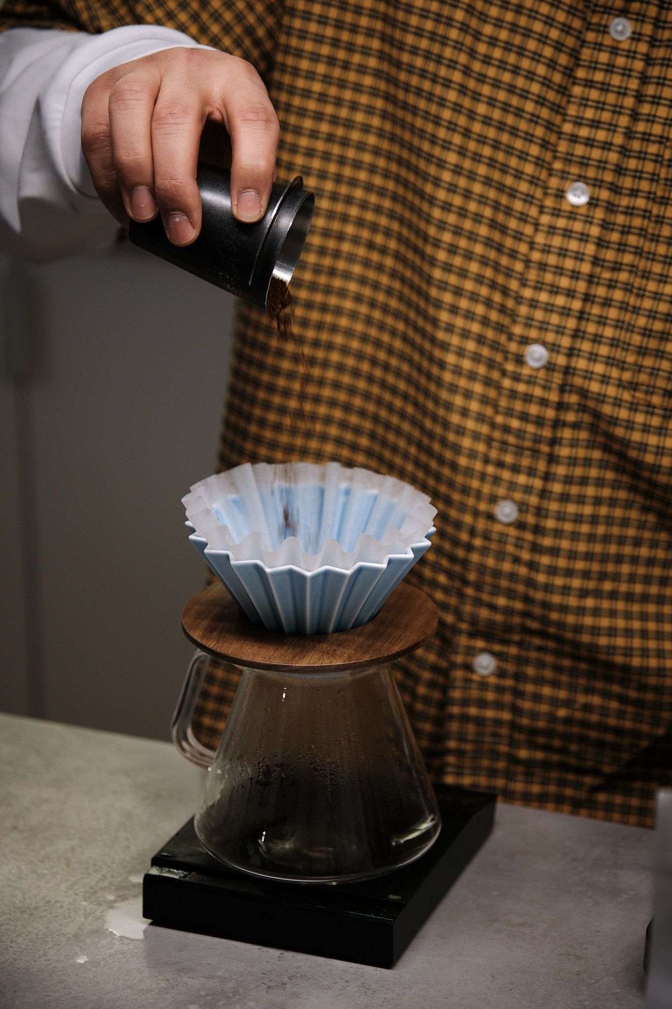 A blue paper coffee filter being placed on top of a Hario V60 pour-over coffee dripper against a checkered background.