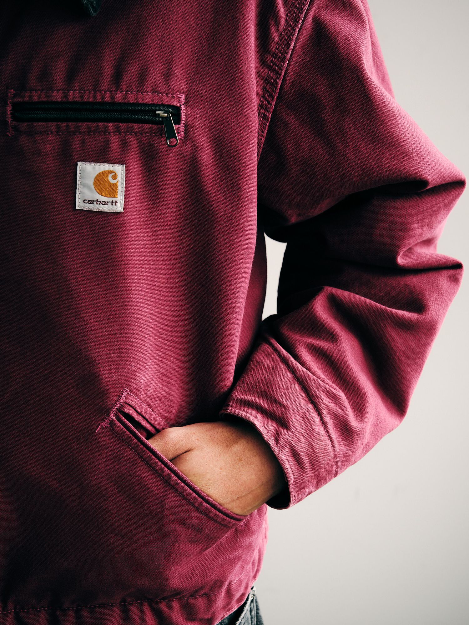 Close-up details of a burgundy Carhartt jacket showing pockets and logo.