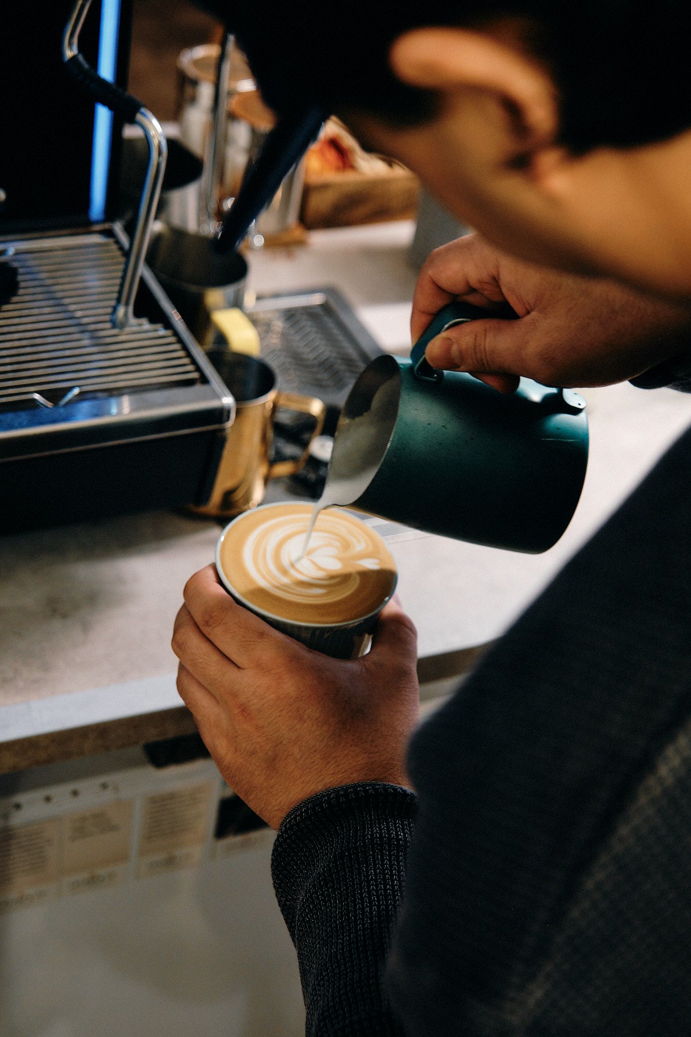 Barista pouring steamed milk into coffee cup creating latte art pattern.