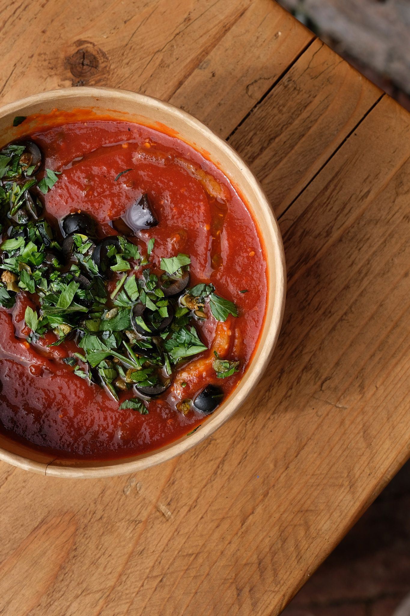 Fresh tomato sauce garnished with vibrant green herbs served in a ceramic bowl on wooden surface.