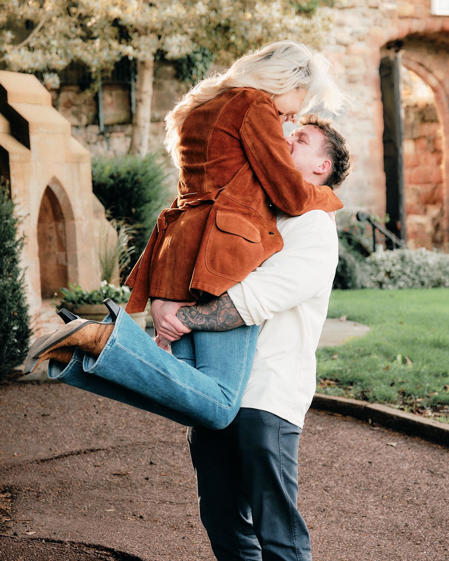 Playful couple embracing outdoors near rustic brick wall setting.
