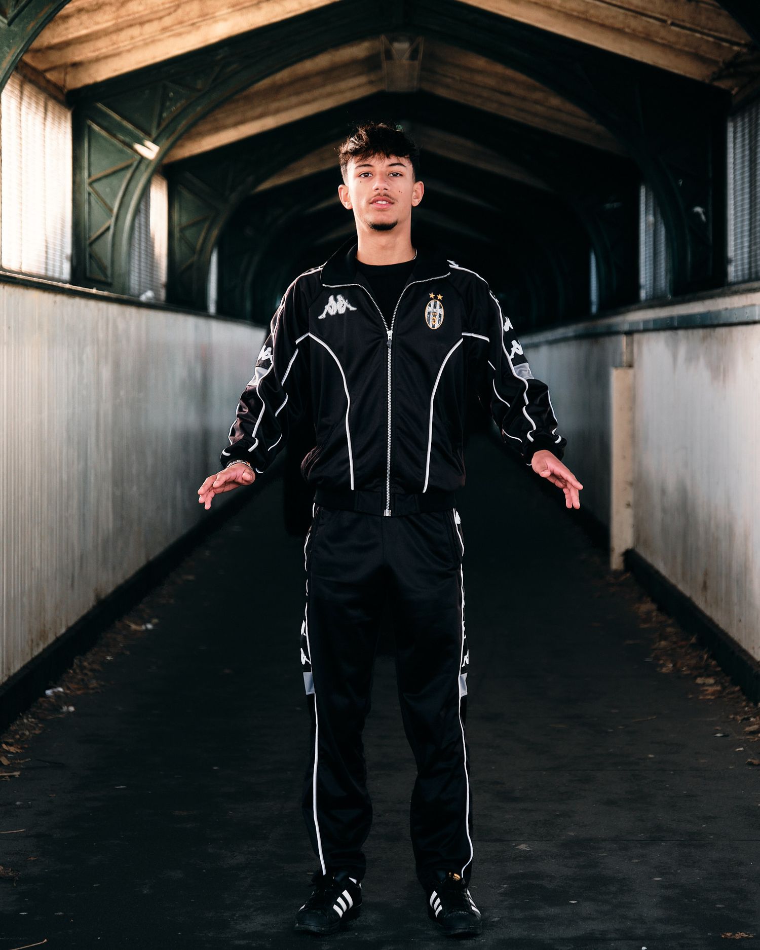 Sports fashion photo of model in Juventus tracksuit with arms spread in concrete tunnel.