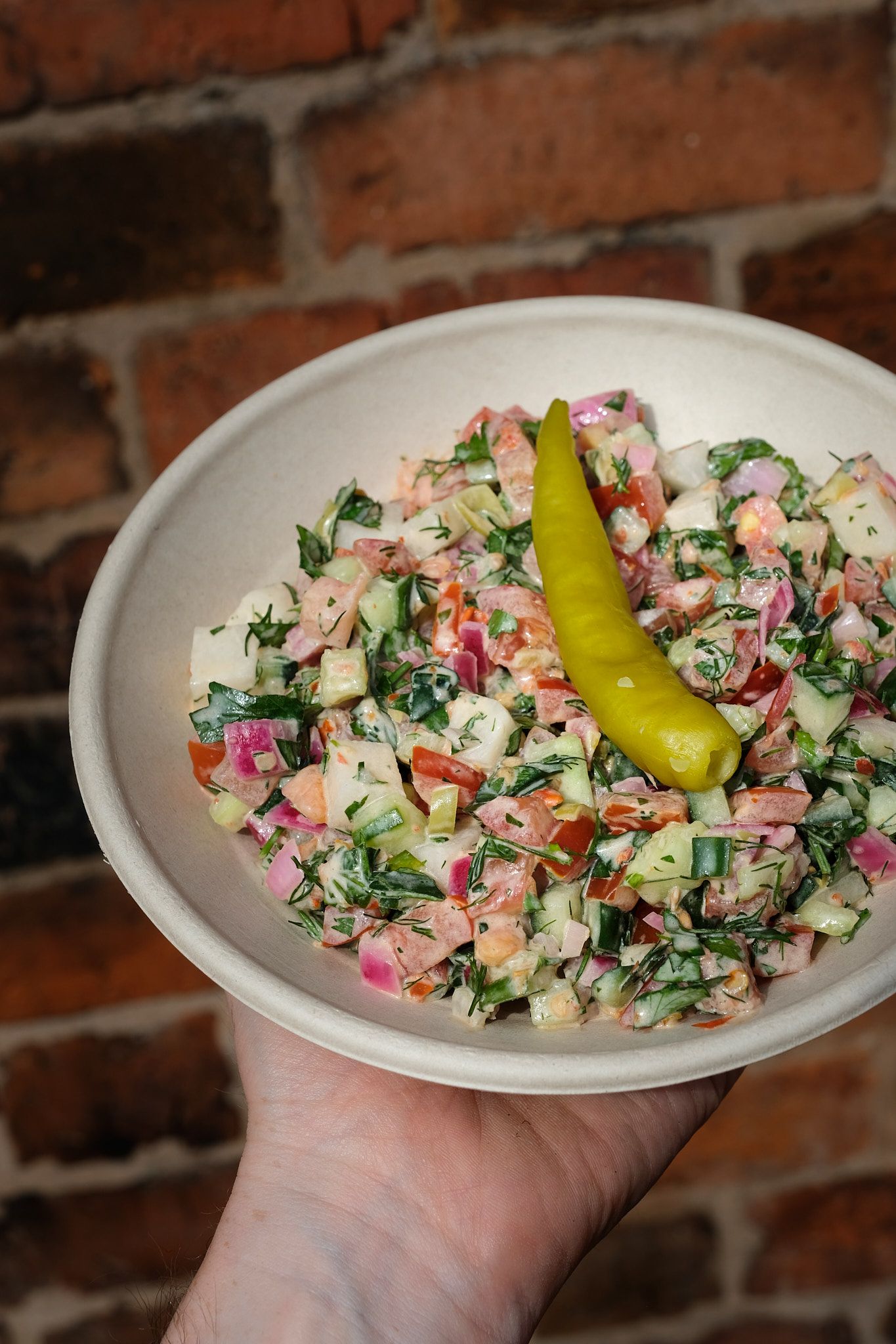 Fresh chopped salad with vegetables and pepperoncini in a white ceramic bowl.