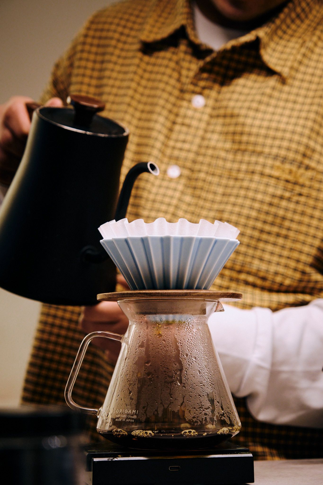 Steam rises from pour-over coffee setup with black kettle and glass carafe.
