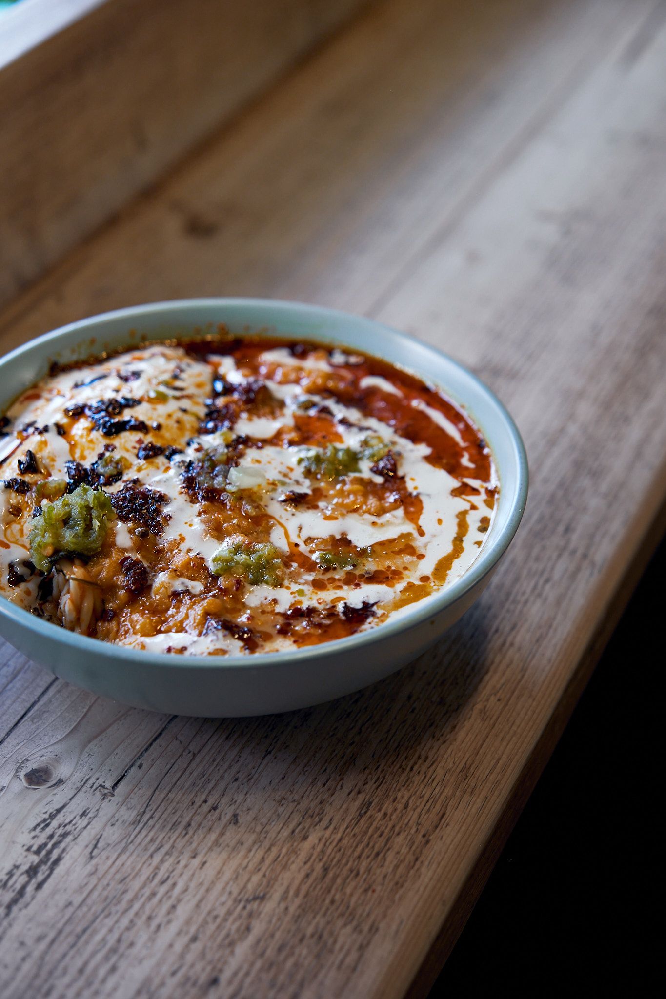 Middle Eastern dip with spiced oil and garnishes in white ceramic bowl on wooden table.