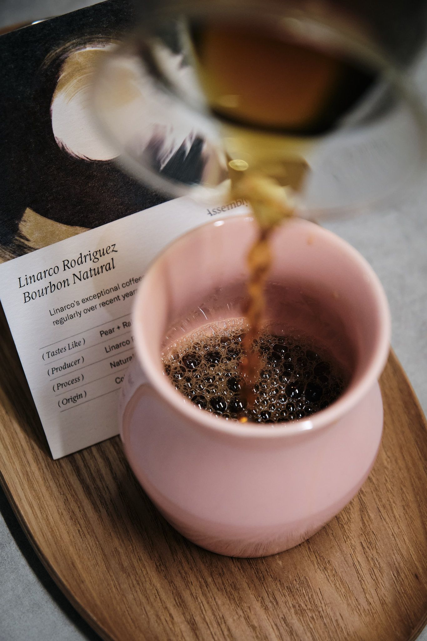 Coffee pouring into pink ceramic cup with brewing details card visible.