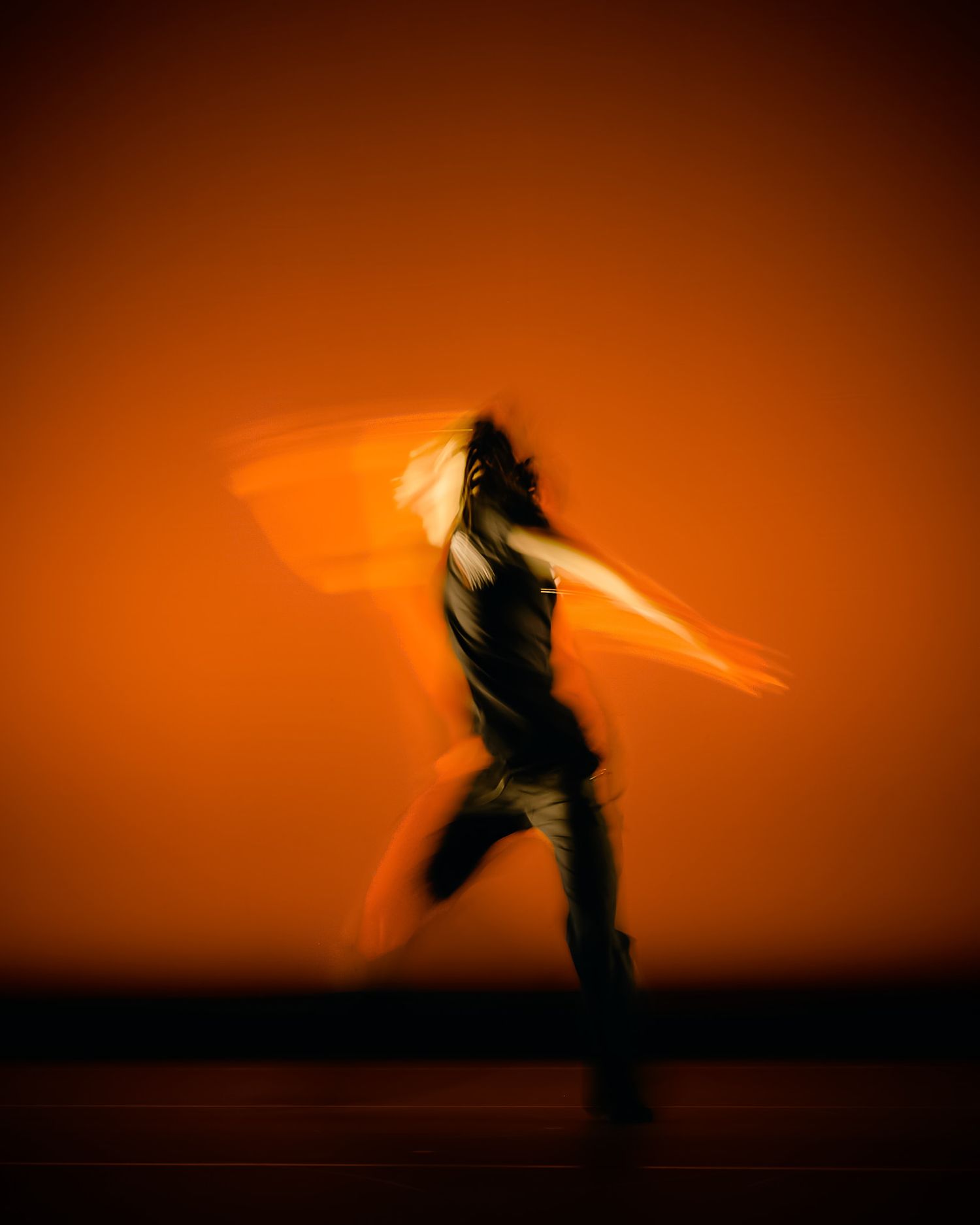 Silhouette of a dancer in motion against a dramatic orange sunset sky creates a striking artistic composition.