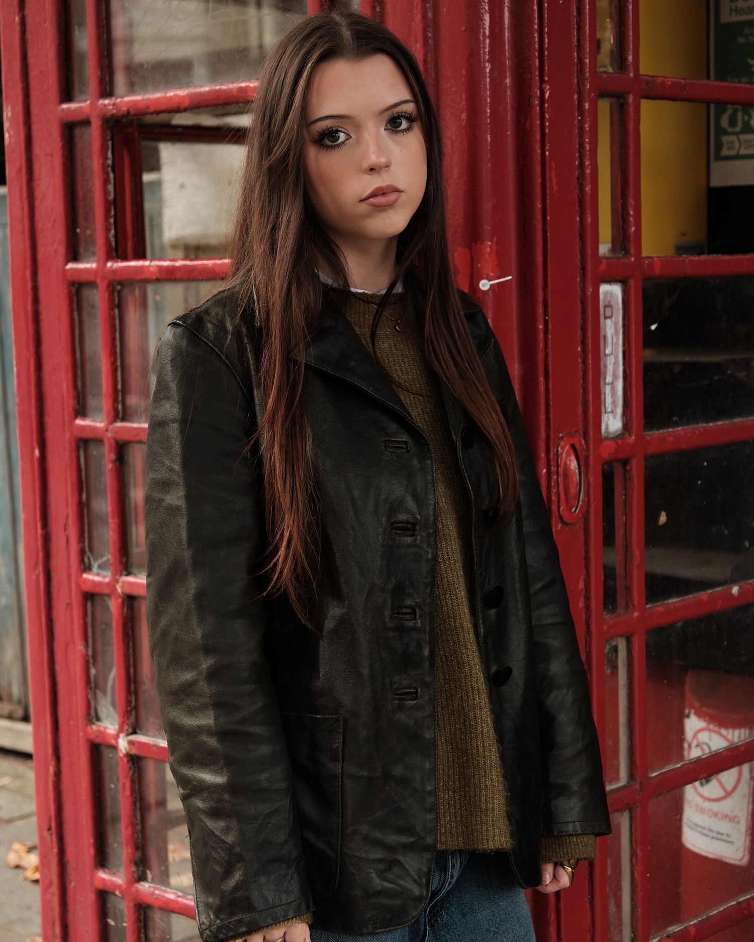 Autumn fashion look featuring leather jacket and long hair against classic red phone booth background.