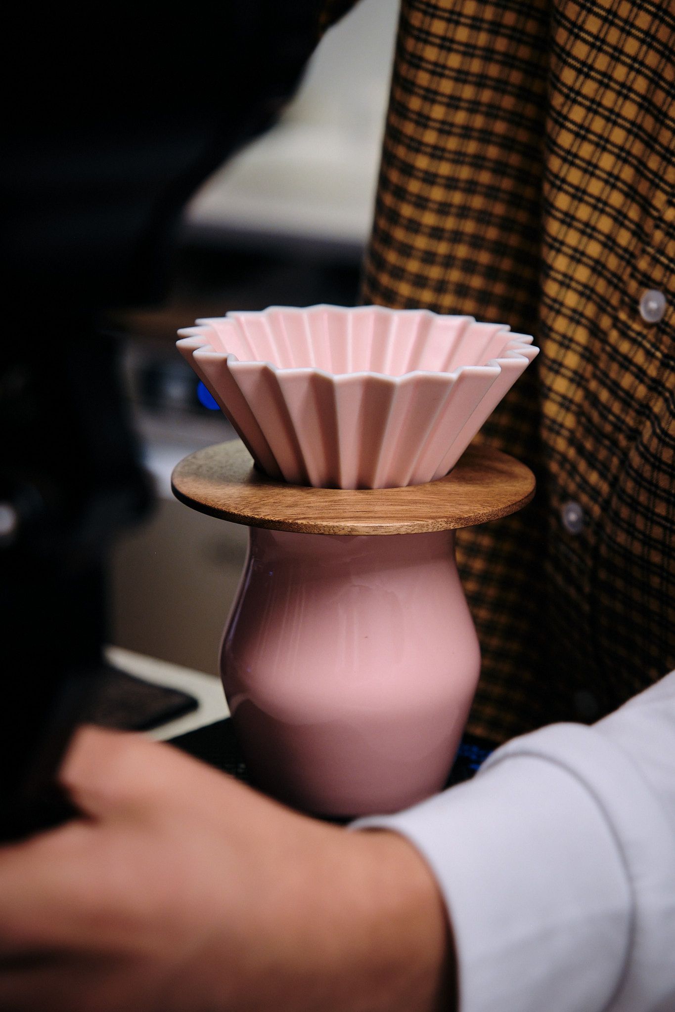 Pink ceramic coffee filter holder with fluted paper filter sits atop a wooden base.