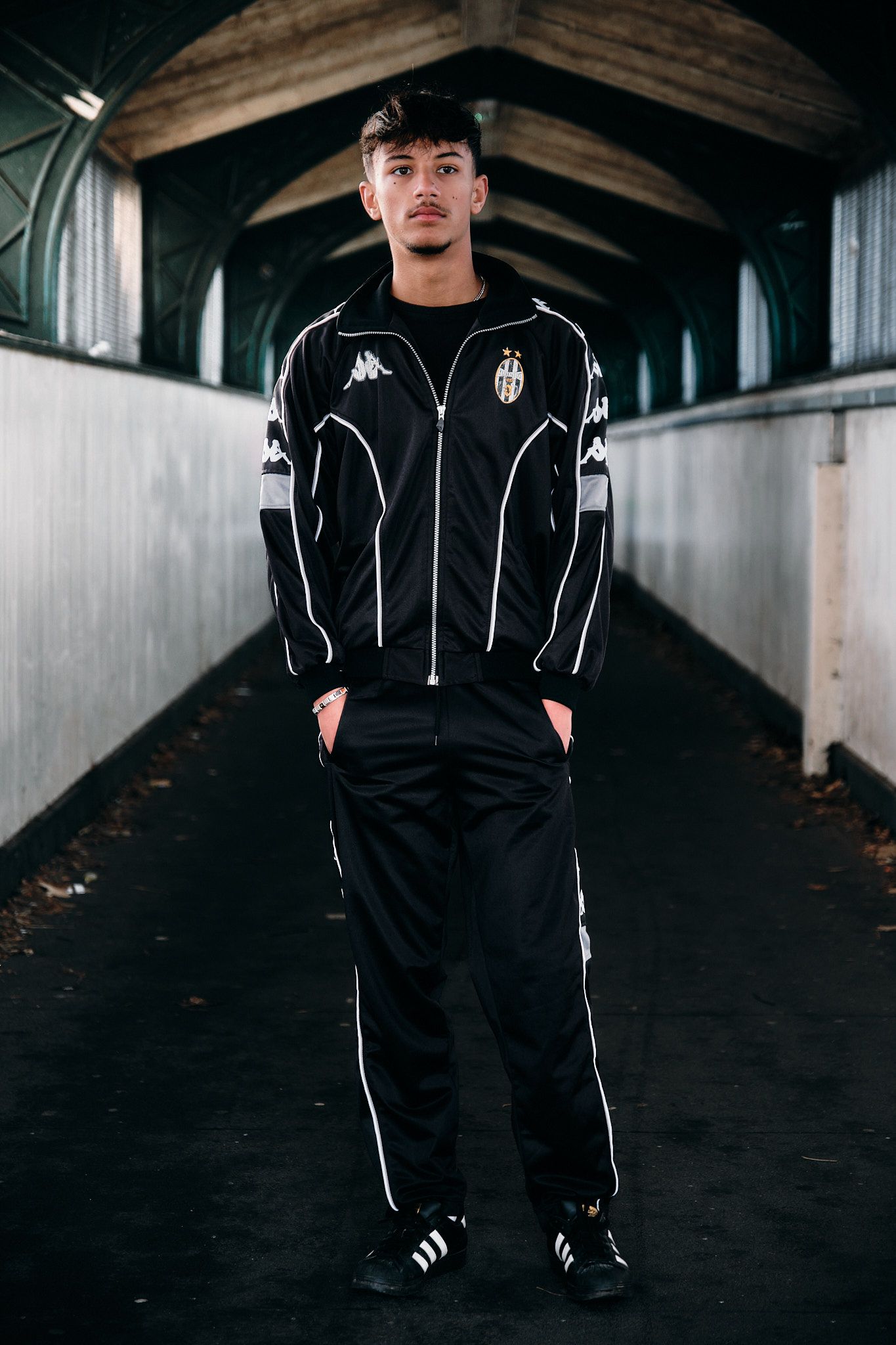 Athletic model in black and white Kappa Juventus tracksuit standing in tunnel.