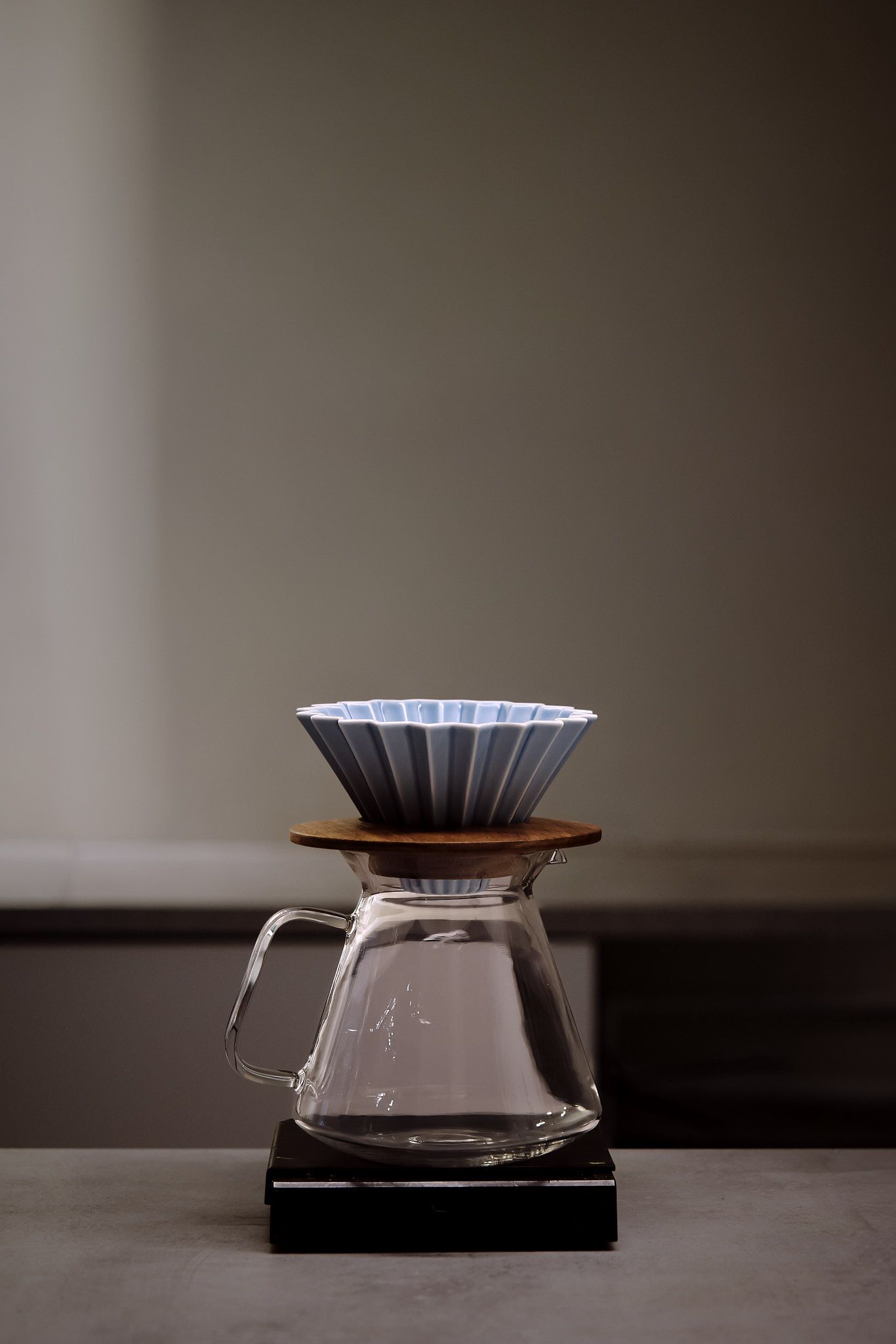 Minimalist coffee brewing setup with glass pour-over dripper on dark surface.