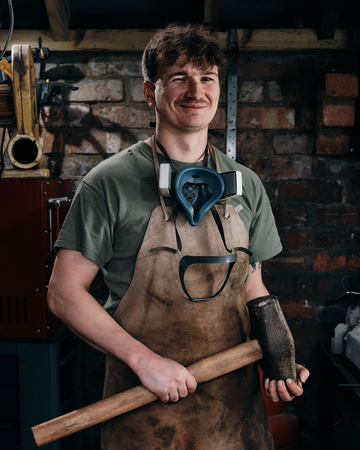Craftsperson in leather apron working in traditional blacksmith workshop with tools.