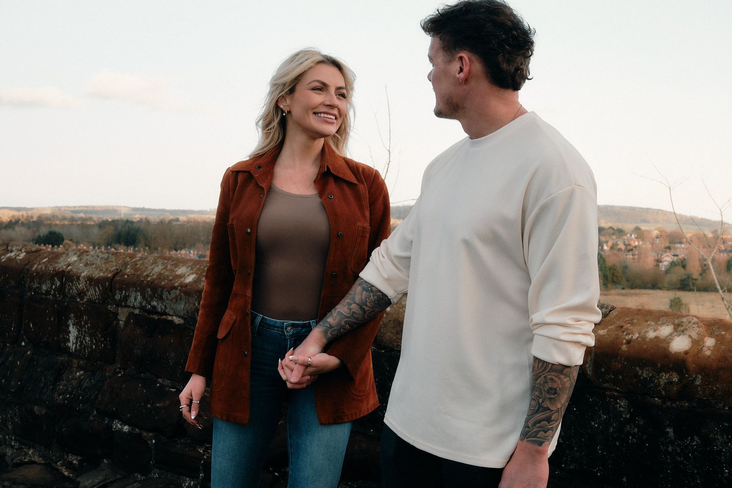 Romantic couple laughing together against bright sunlit background in casual autumn attire.