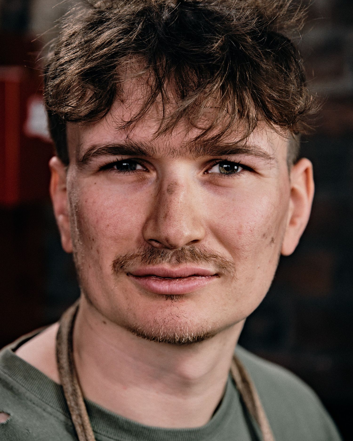 Portrait of person in olive shirt and safety glasses in workshop setting.