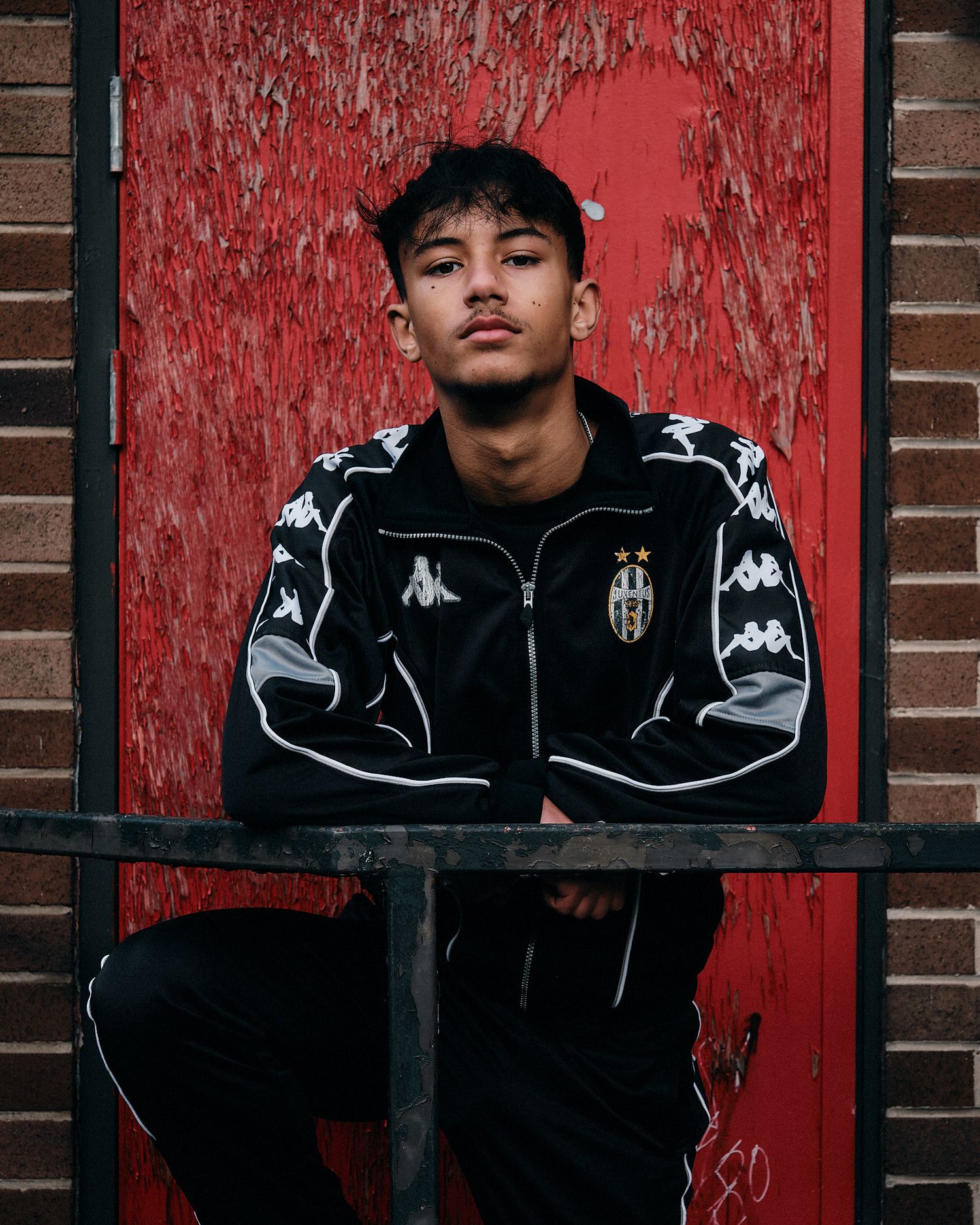 Urban fashion portrait against red weathered door showing black Kappa sportswear.
