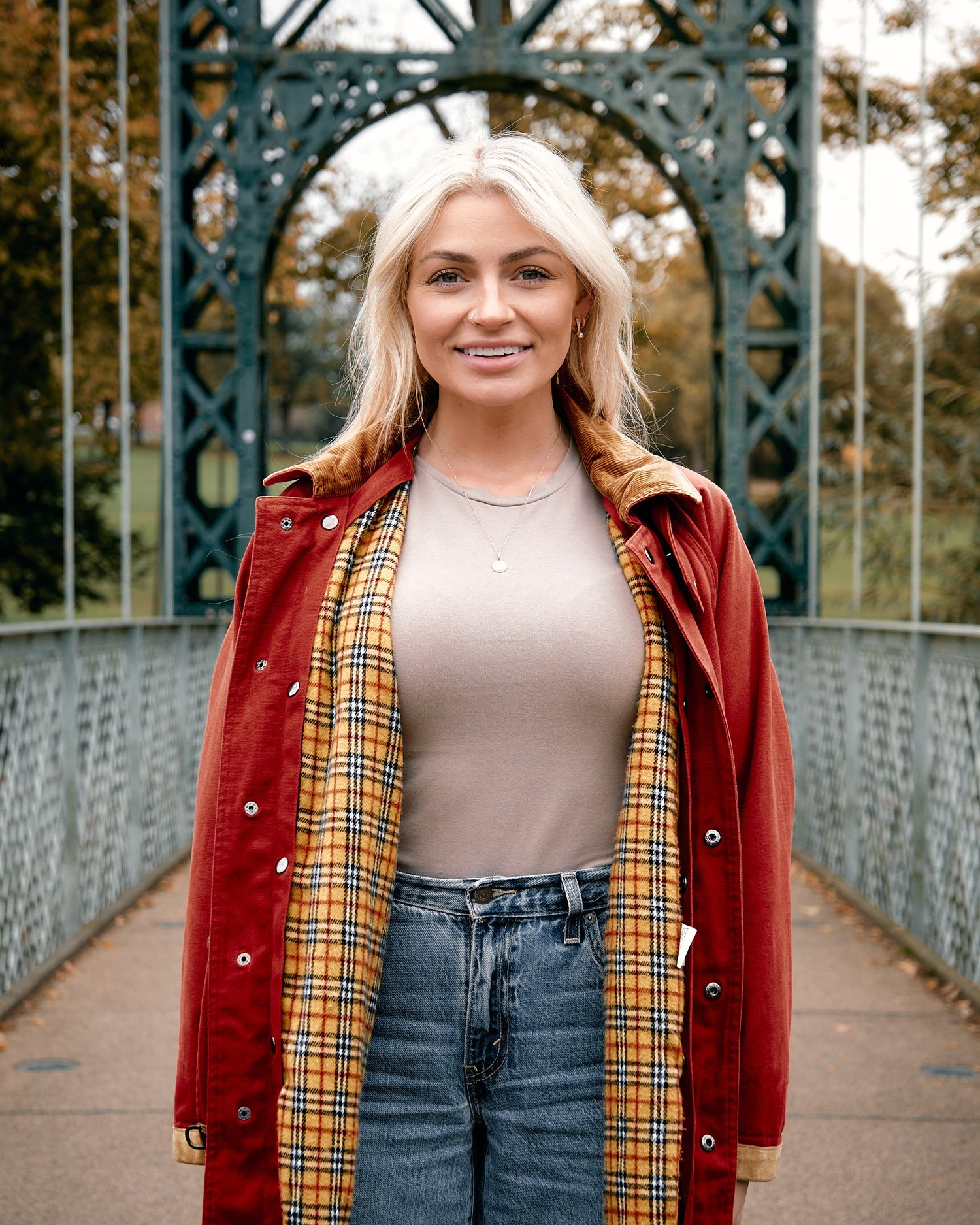 A casual autumn outfit featuring a red corduroy jacket with plaid lining and jeans on a bridge.