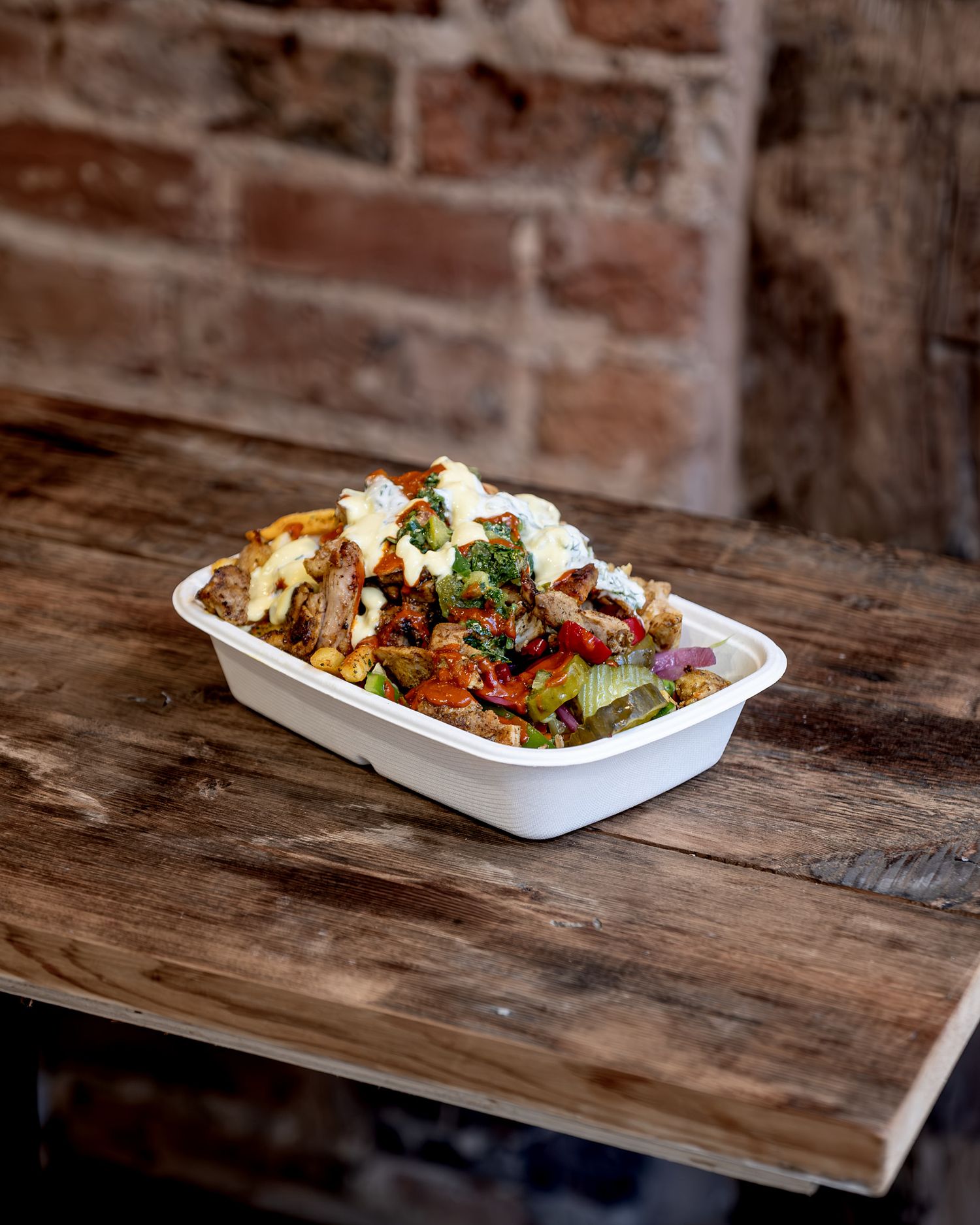 Mediterranean food plated in white takeout containers on rustic wooden table.