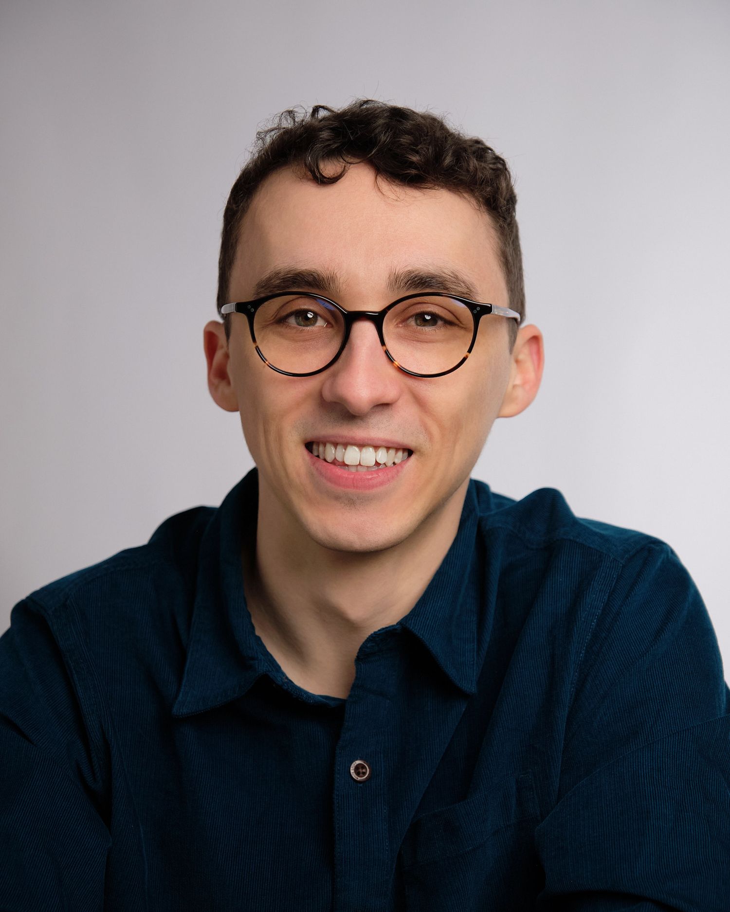 A person wearing glasses and a navy sweater smiles warmly while posing for a series of headshots against a light background.