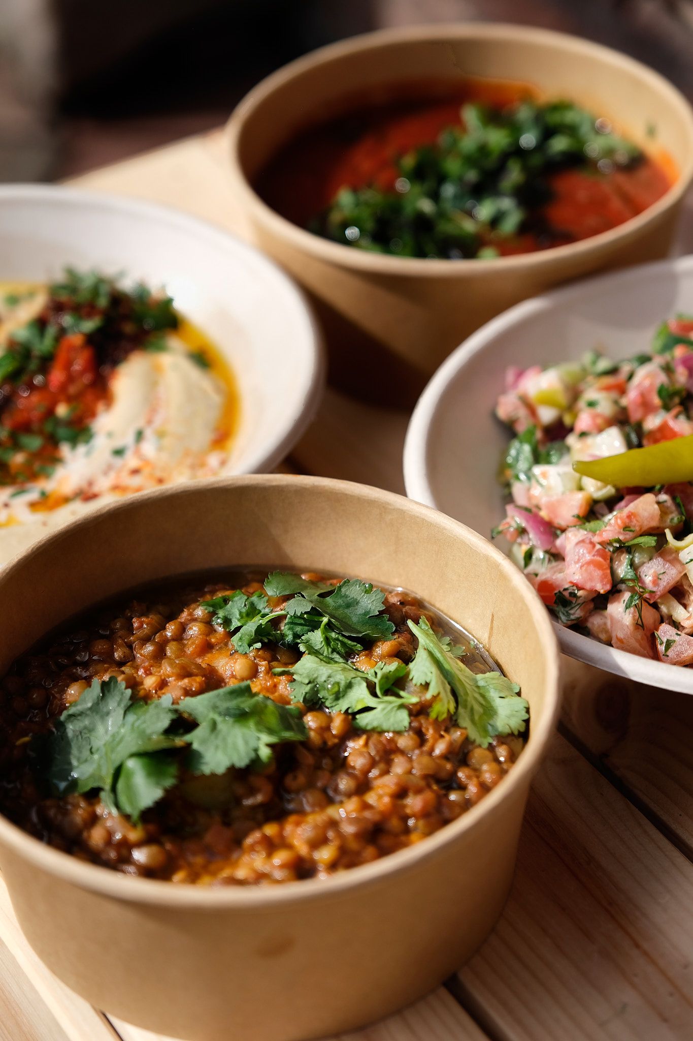 Row of beige ceramic bowls filled with colorful Mediterranean dishes and garnishes on rustic wooden table.