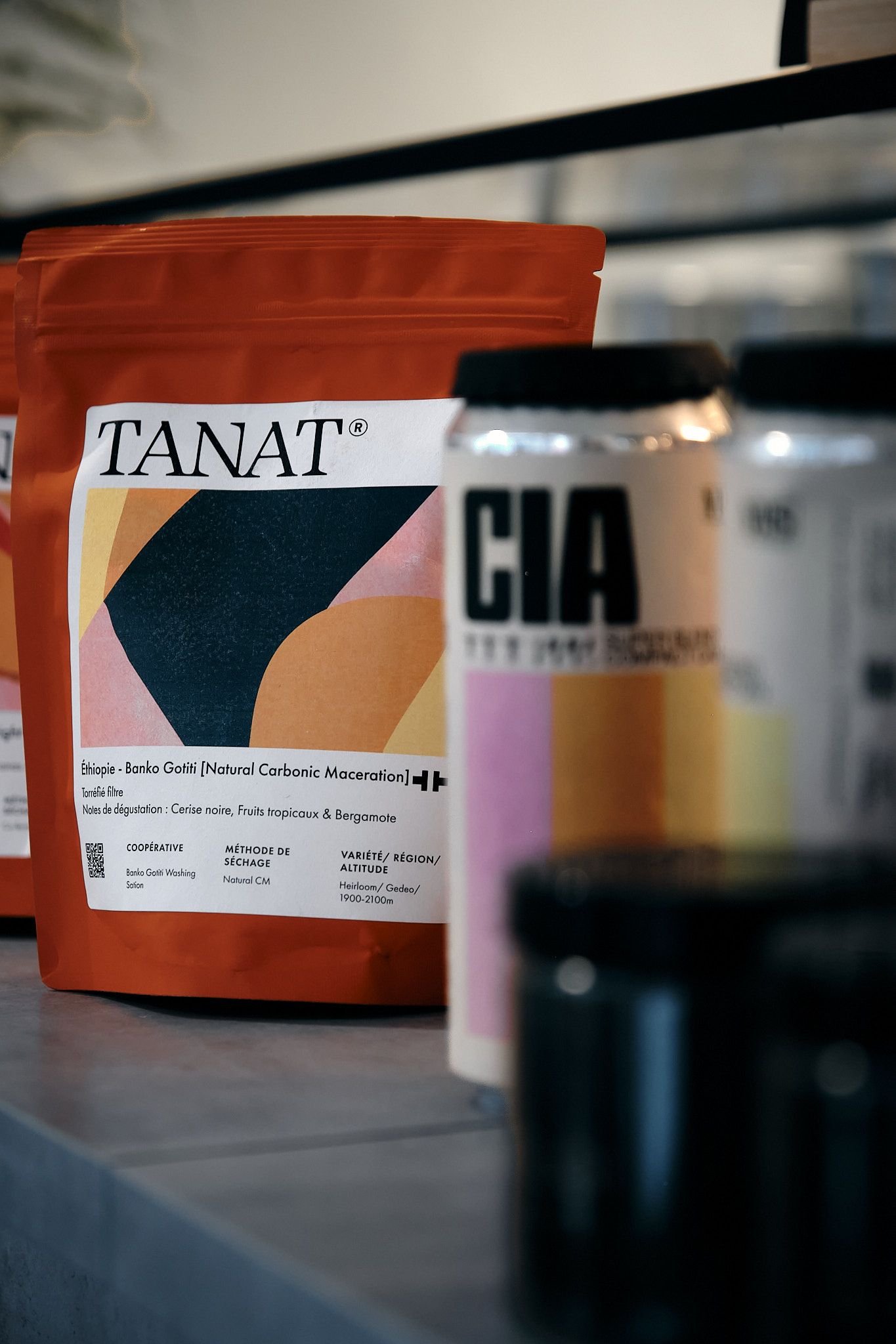 Orange TANAT coffee bag with abstract geometric design next to blurred containers.