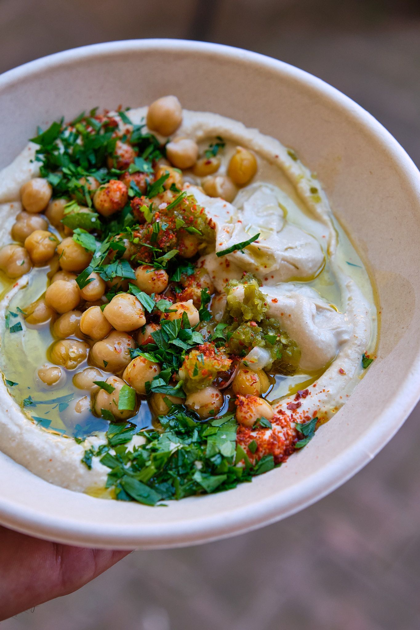 Creamy hummus bowl topped with chickpeas, herbs, and olive oil in white ceramic dish.