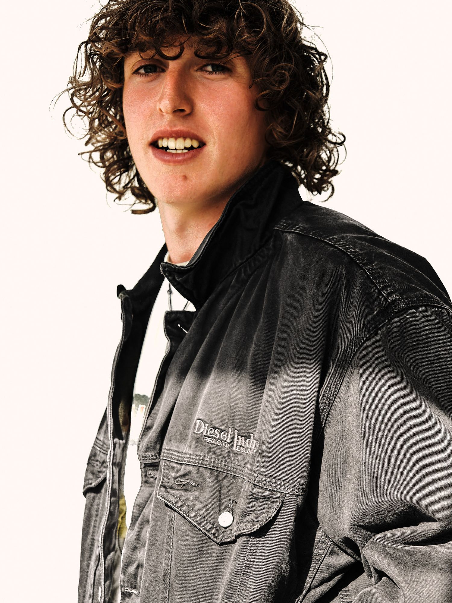Person wearing a black denim jacket with curly hair against white background in artistic portrait series.