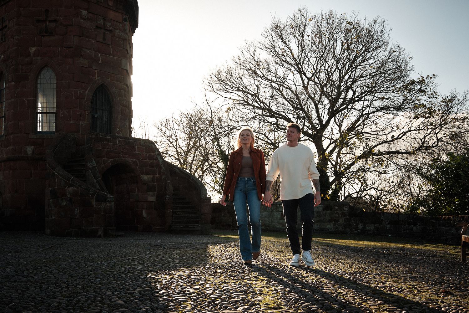 Silhouettes of people walking along a stone wall at sunset.