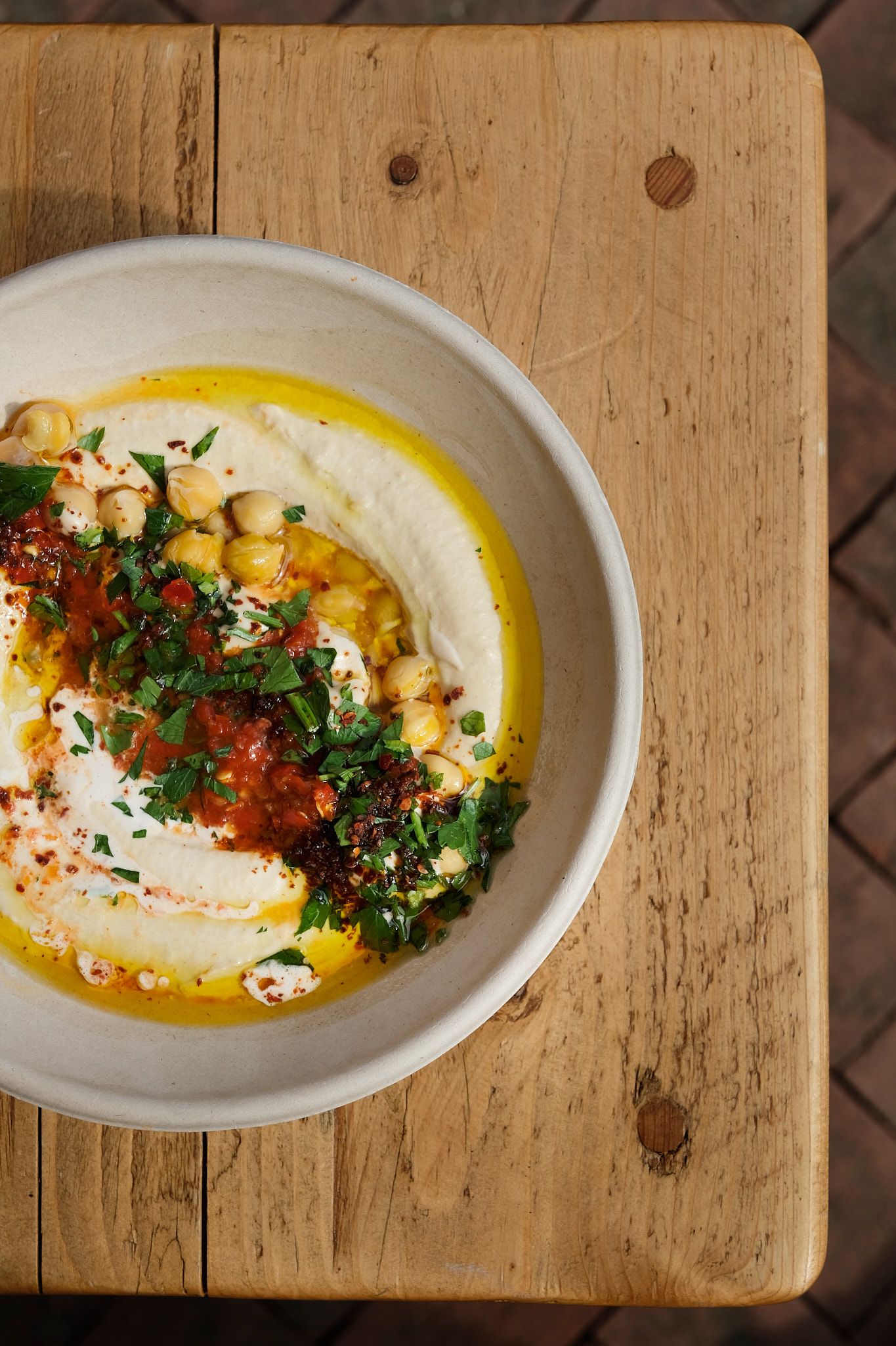 Homemade hummus topped with olive oil, paprika and fresh herbs on wooden board.