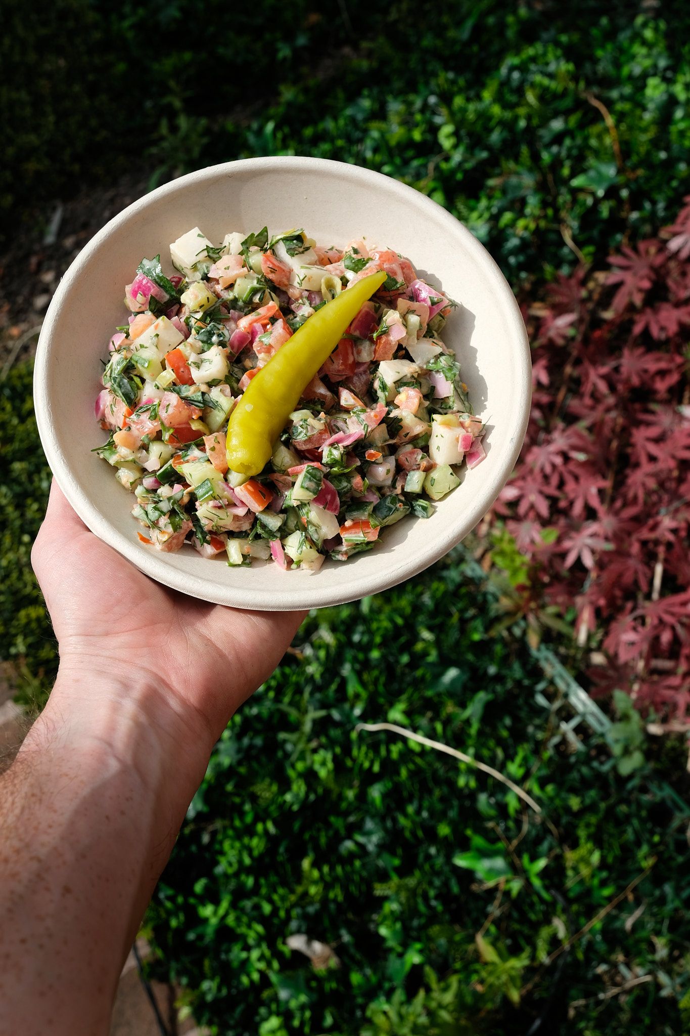 Mediterranean chopped salad with pepperoncini in a white bowl outdoors.