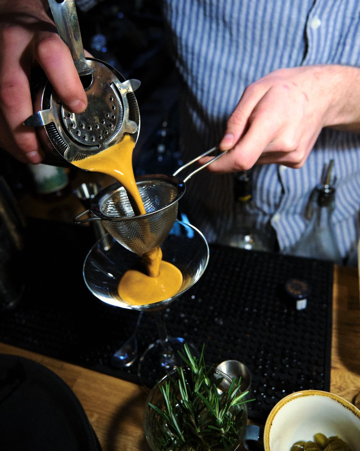 Pouring a golden liquid into a bowl with fresh herbs and ingredients for cooking.