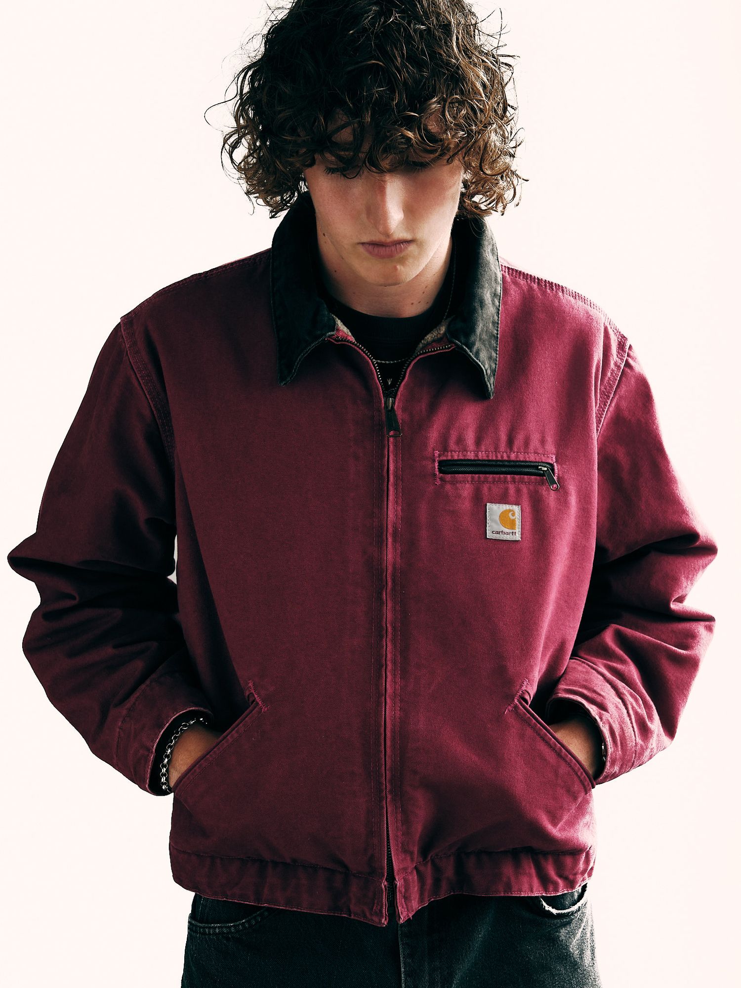 Person wearing a burgundy Carhartt jacket against white background.