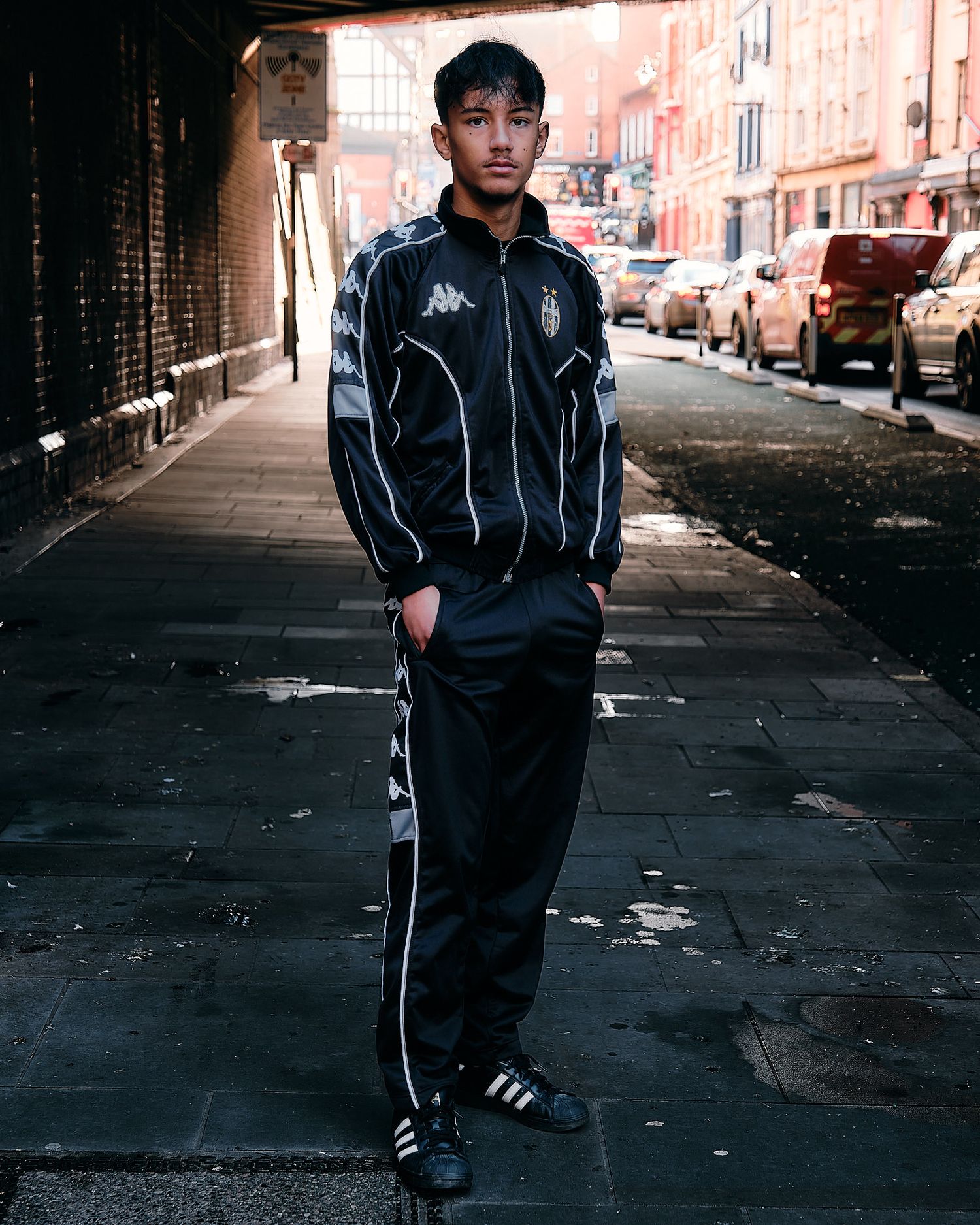 Street style photo of black Kappa tracksuit on urban sidewalk.