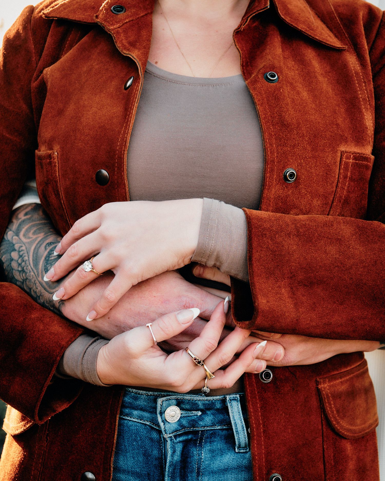 Close-up of brown suede jacket and jewelry details against denim.